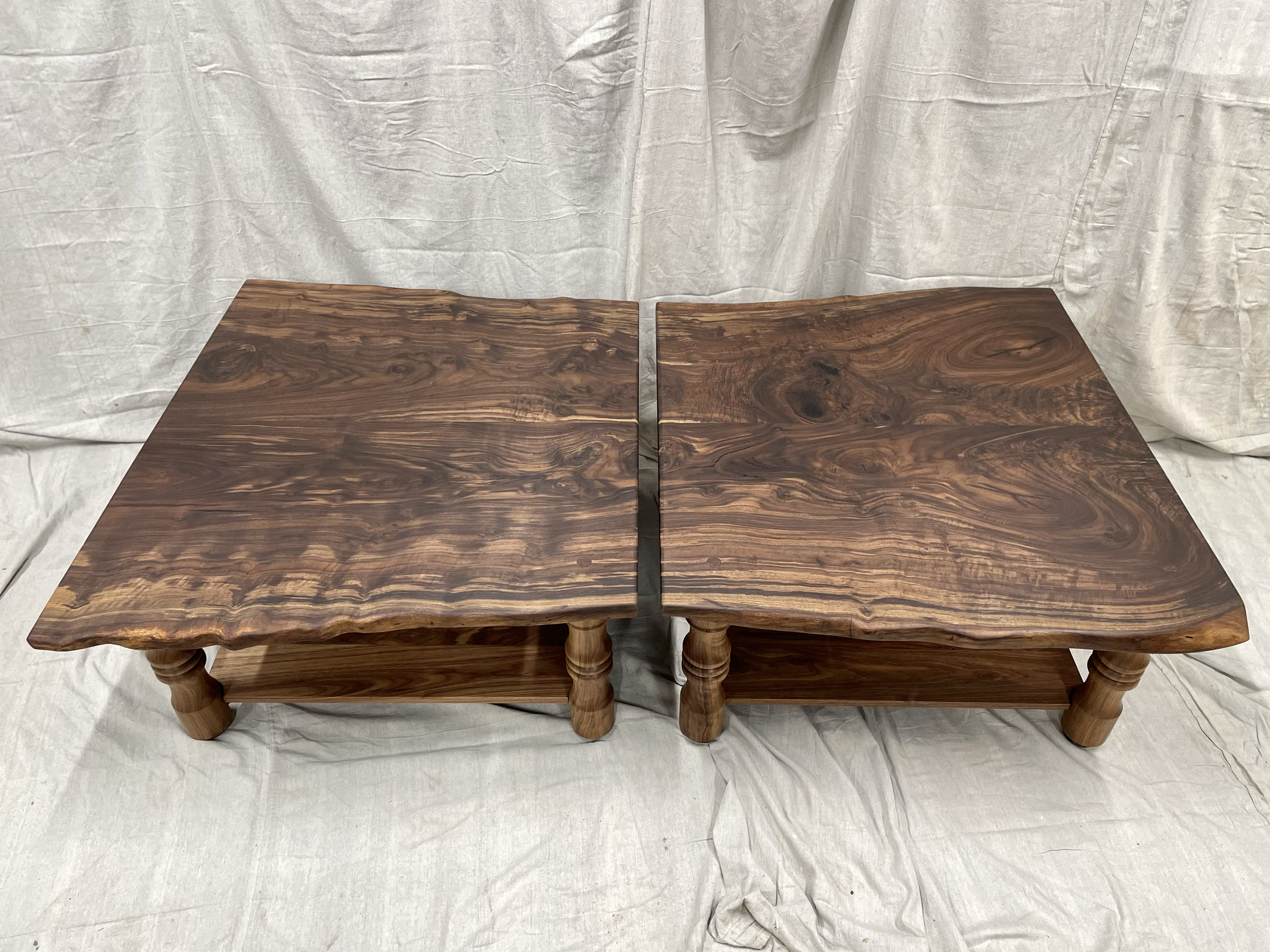 Two handcrafted wooden tables with natural finish and live edge, placed side by side on a white fabric background.