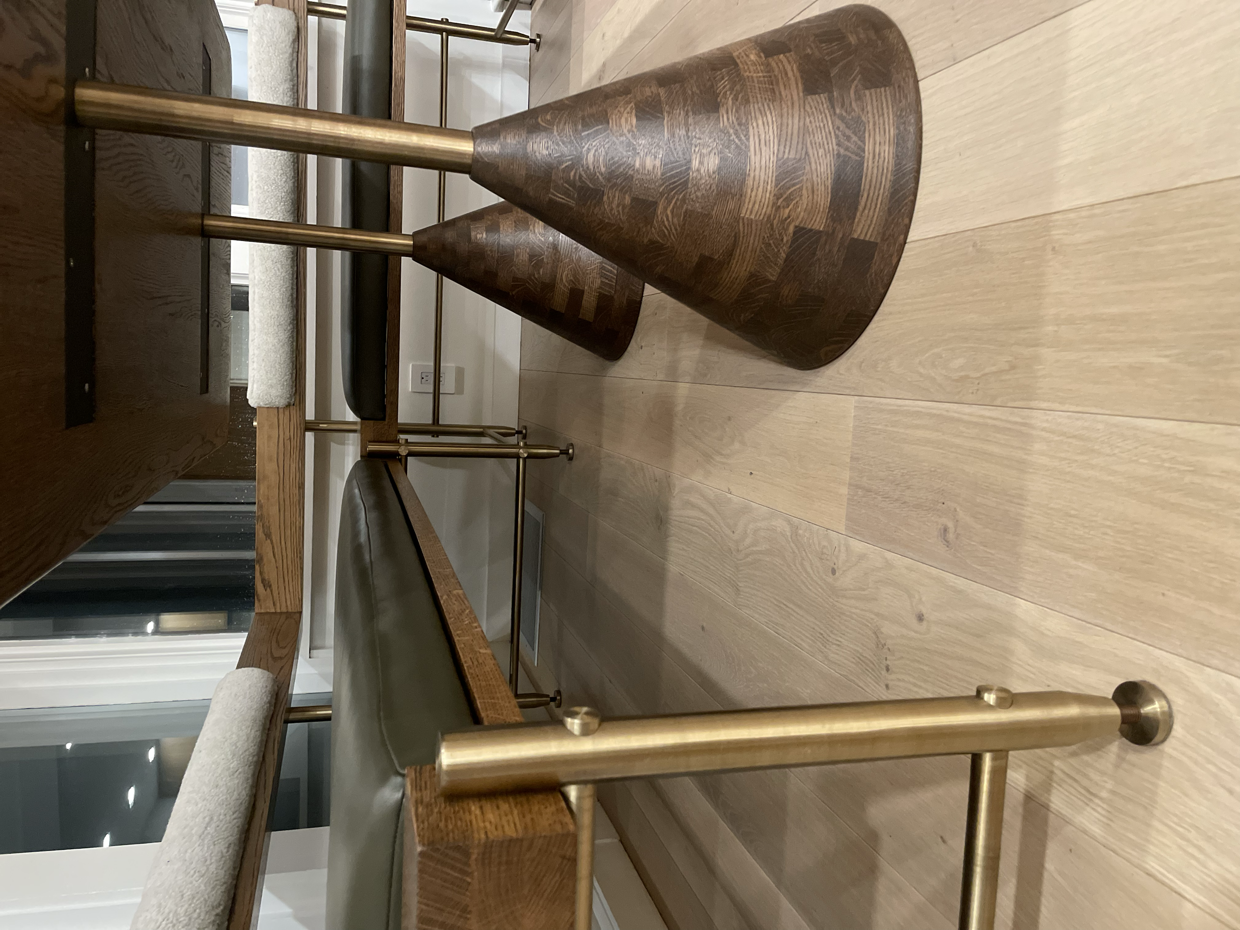 Two wooden cones with a dark wood pattern and brass rods at their narrow ends, placed on a wooden floor.