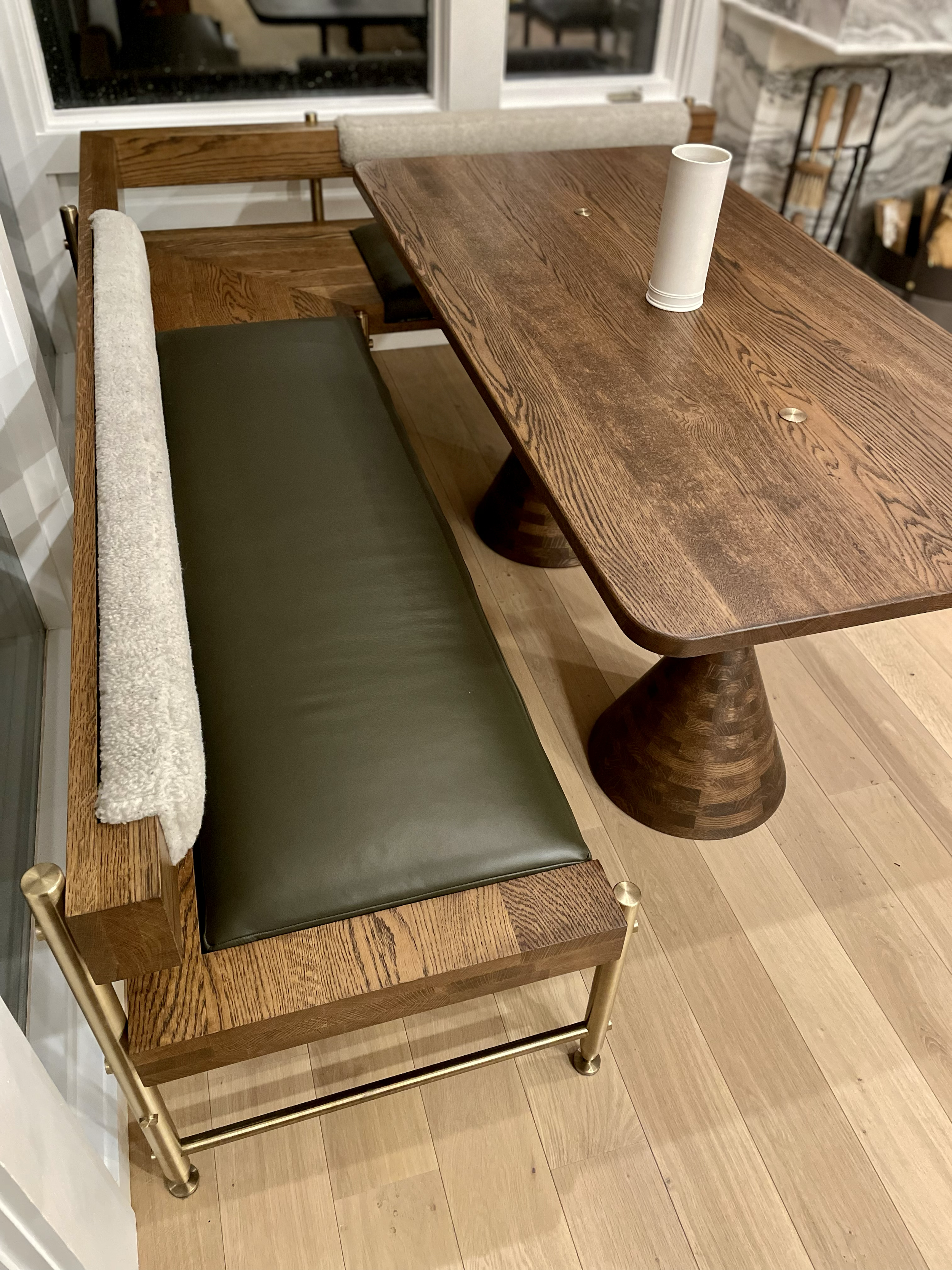 A wooden dining table with a cylindrical paper towel holder and a bench with a green cushion and brass frame.