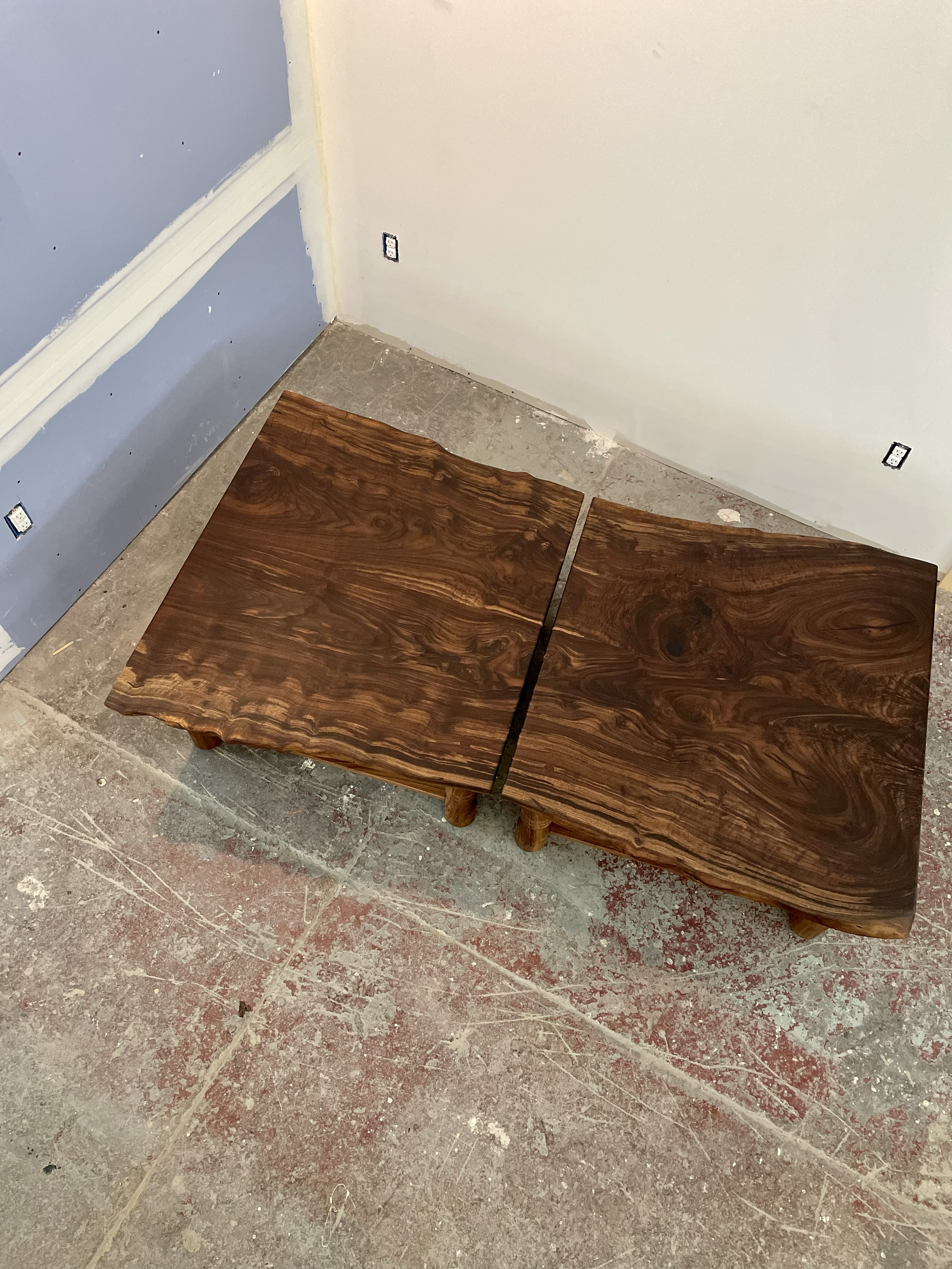 Wooden table with a unique, live edge design placed on a concrete floor in a room under construction or renovation.