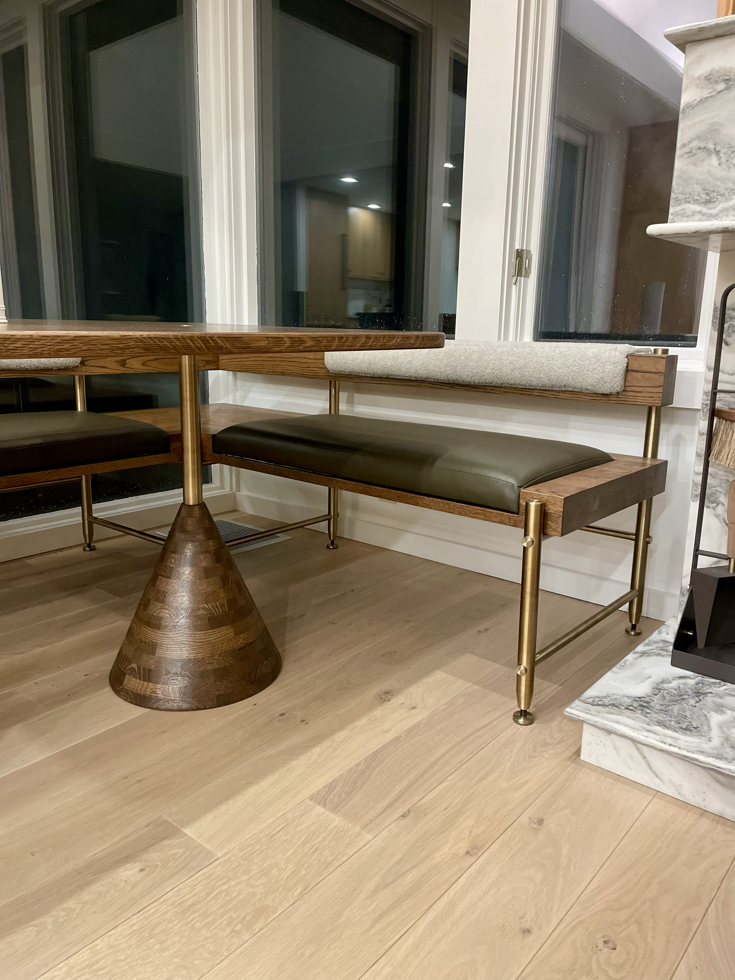 Interior scene with a wooden and metal bench with a cushion, a wooden table, and a marble fireplace surround.