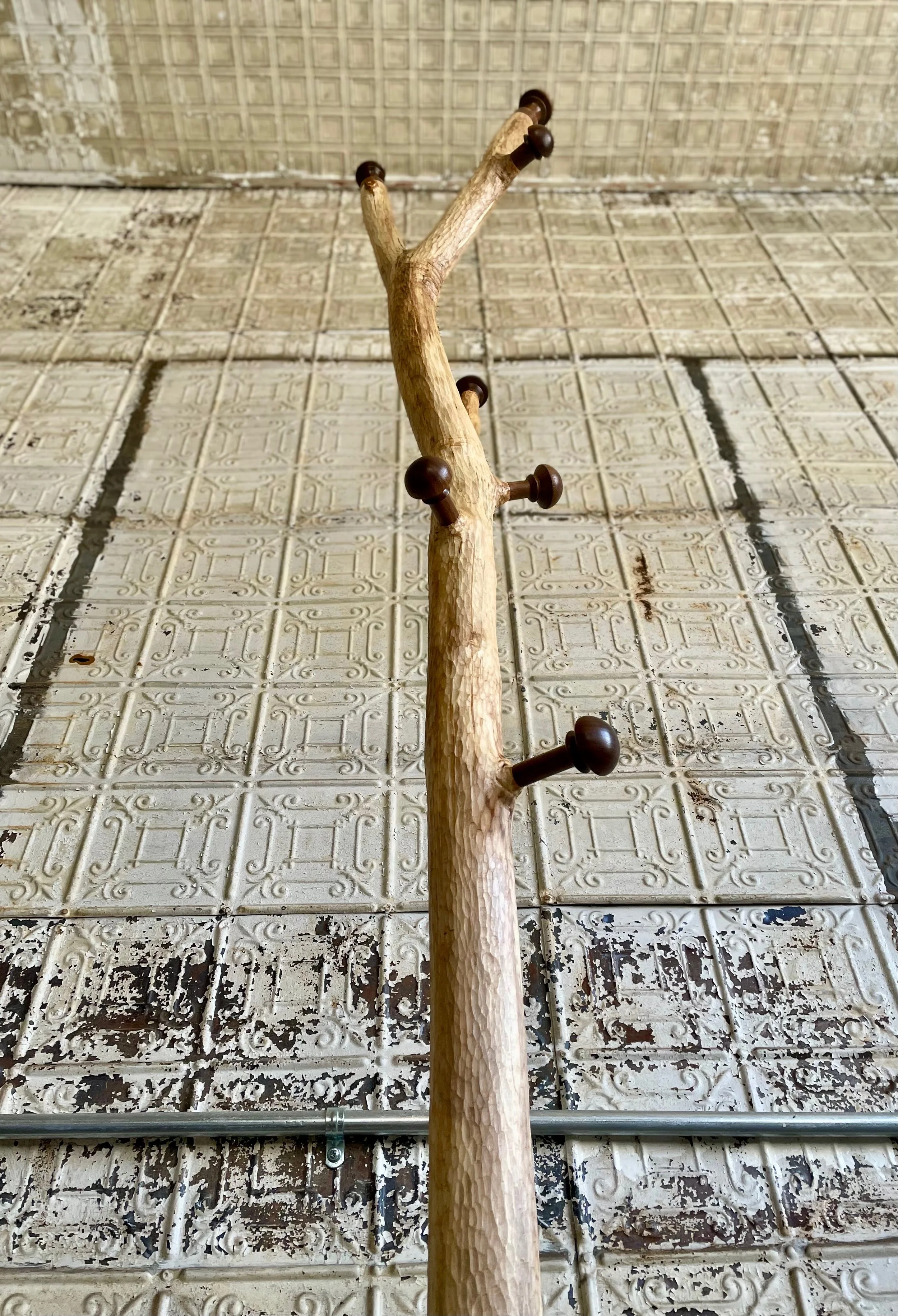 A wooden coat rack with multiple hooks is mounted on a worn, textured ceiling with decorative tiles.