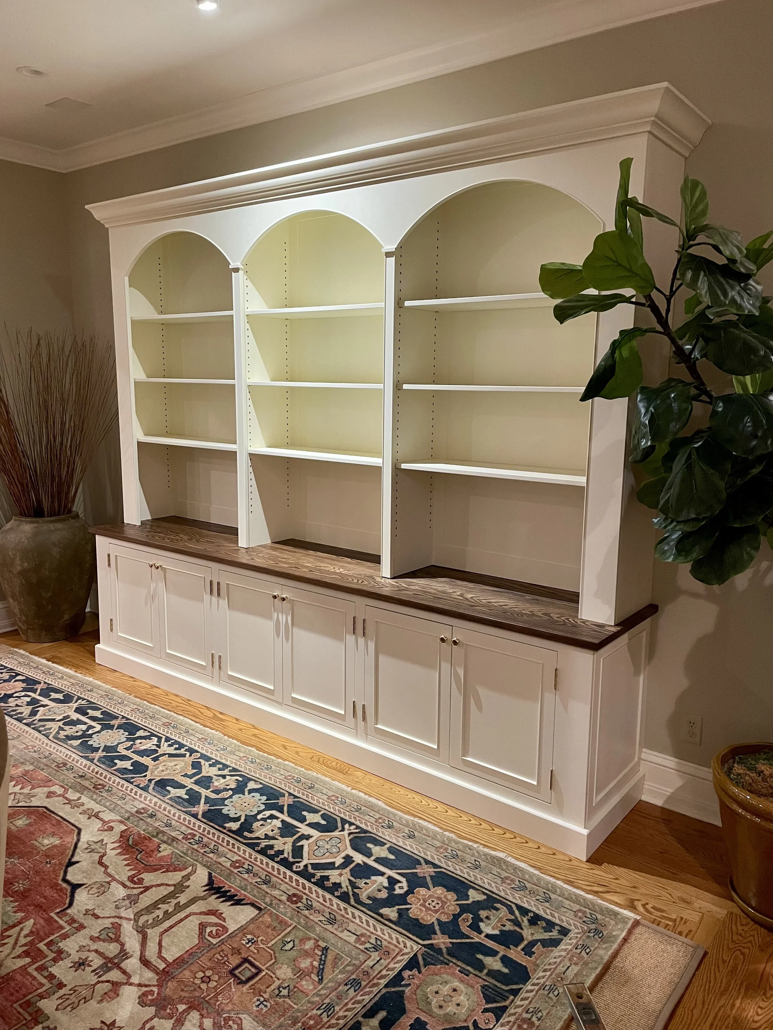 White wooden hutch with dark wood countertop and open shelves in living room, next to large potted plant and patterned rug.