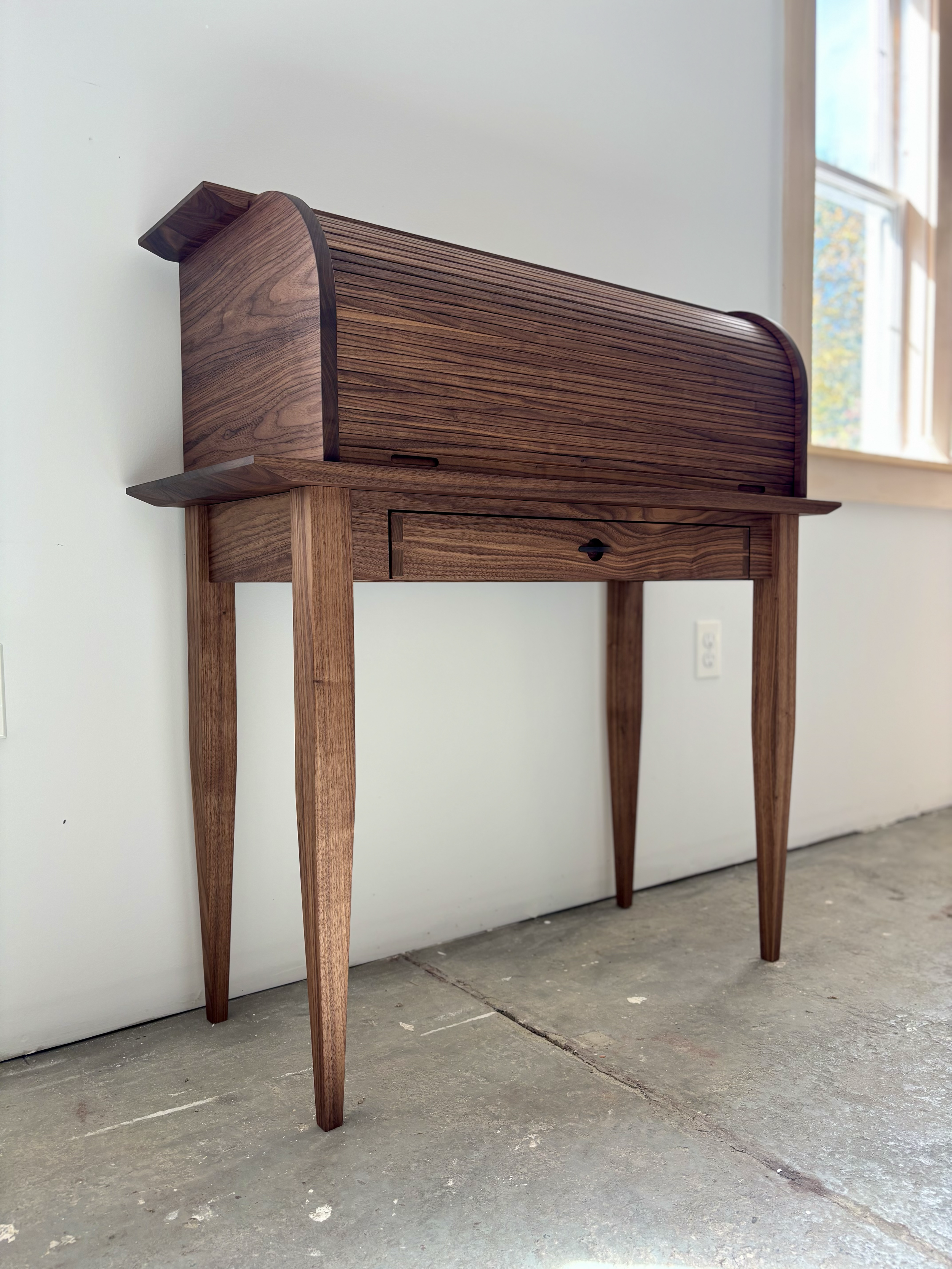 Elegant mid-century modern wooden desk with curved top, against a white wall near a window.
