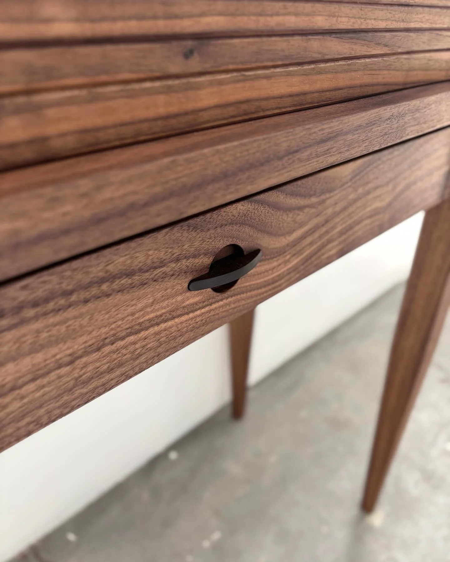 Close-up of a custom walnut desk or table with a drawer, showing a black drawer pull.