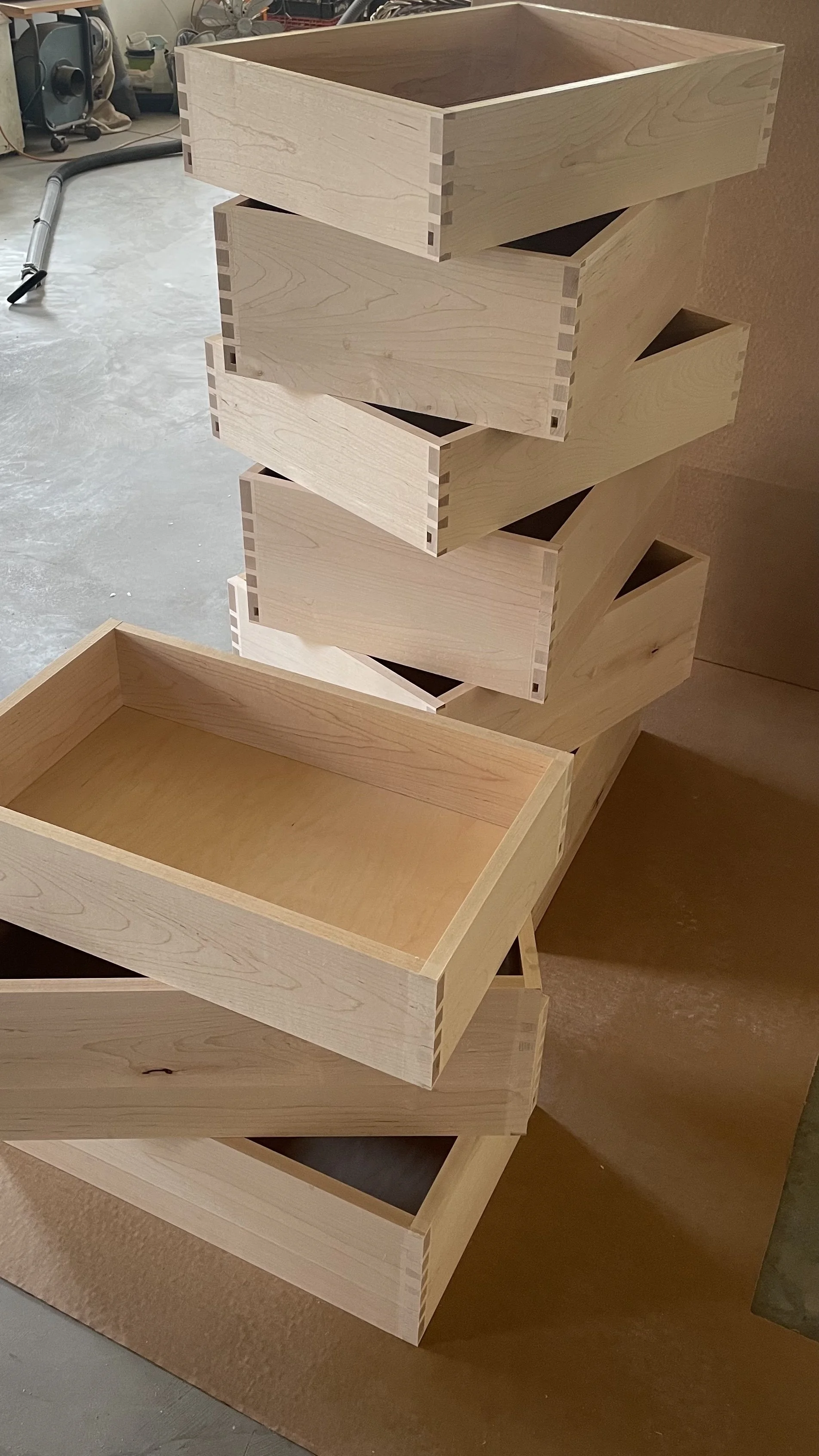 Stacked unfinished wooden drawers or boxes with dovetail joints in a woodworking shop.