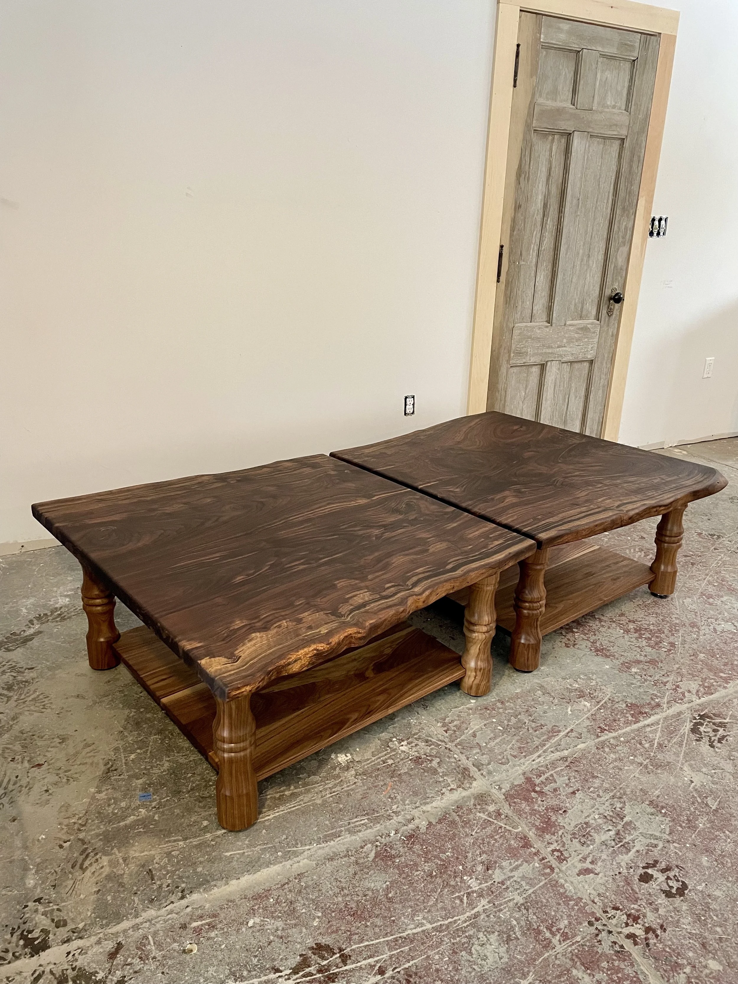 A wooden coffee table with a natural, live-edge design on the top and a lower shelf, situated on a concrete floor in an unfinished room.