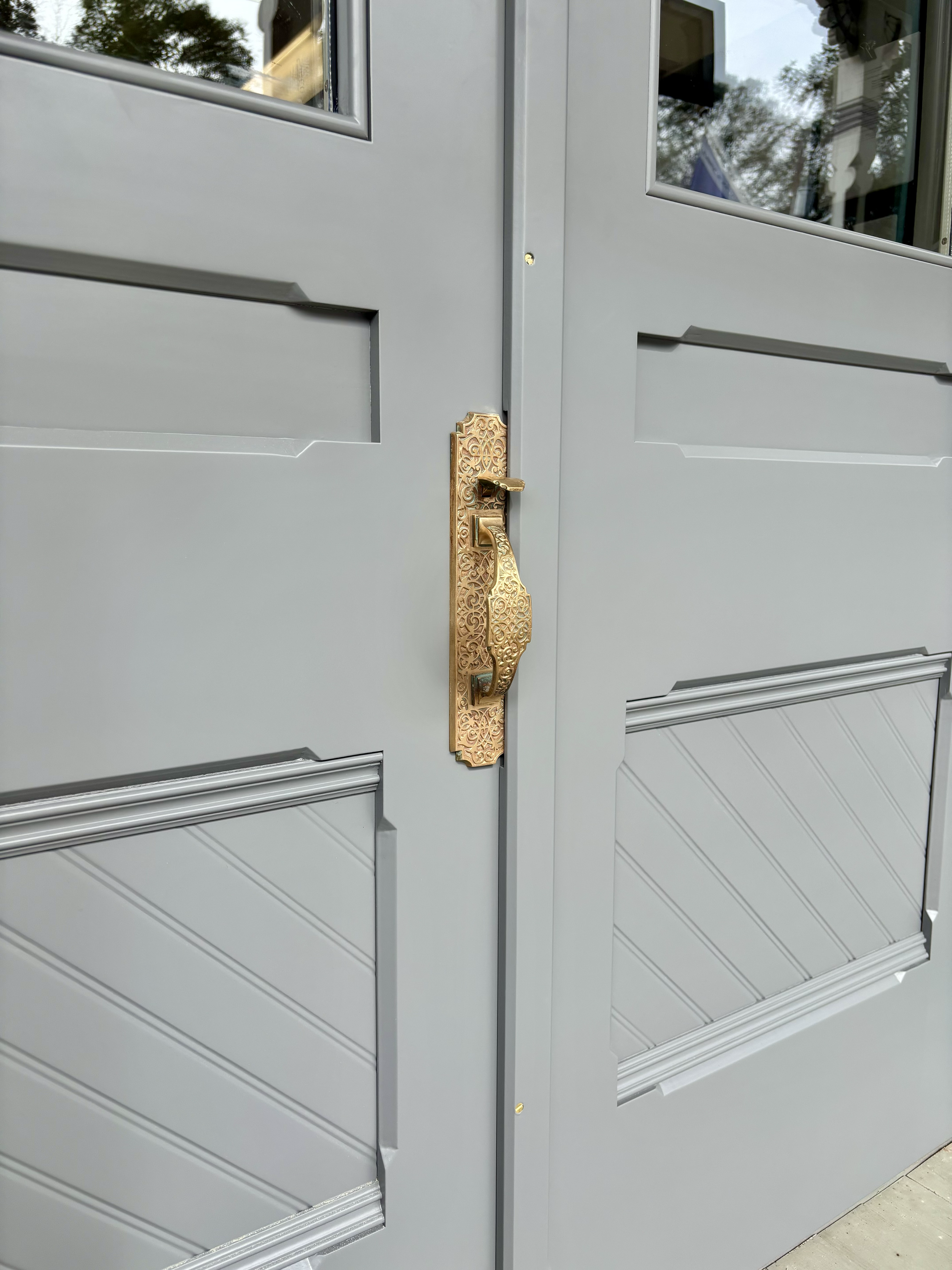 Close-up of a gray double door with ornate brass handle and lock.