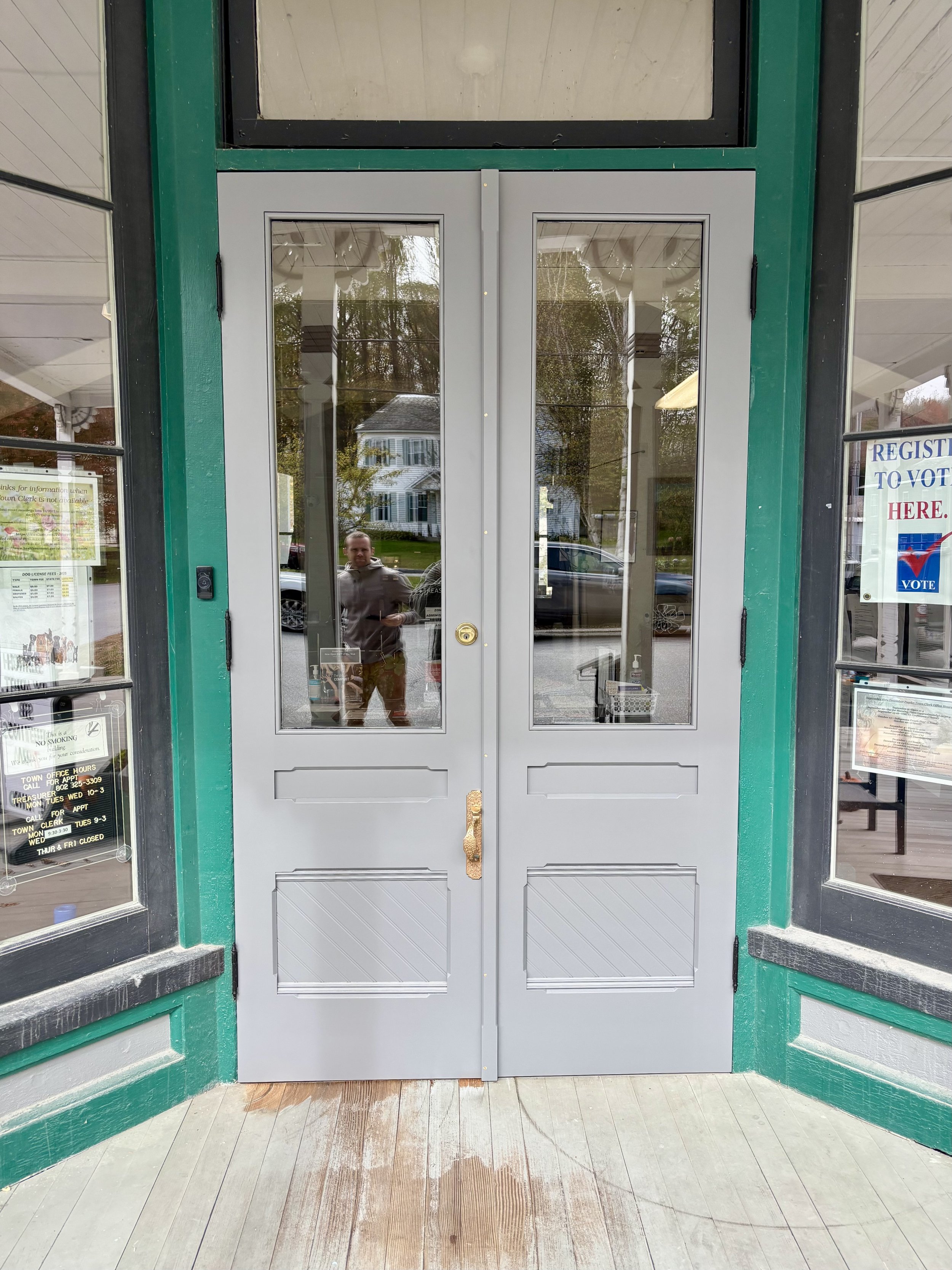 Double glass doors with gray frames and gold handles, leading into a building, with signs and windows on either side.