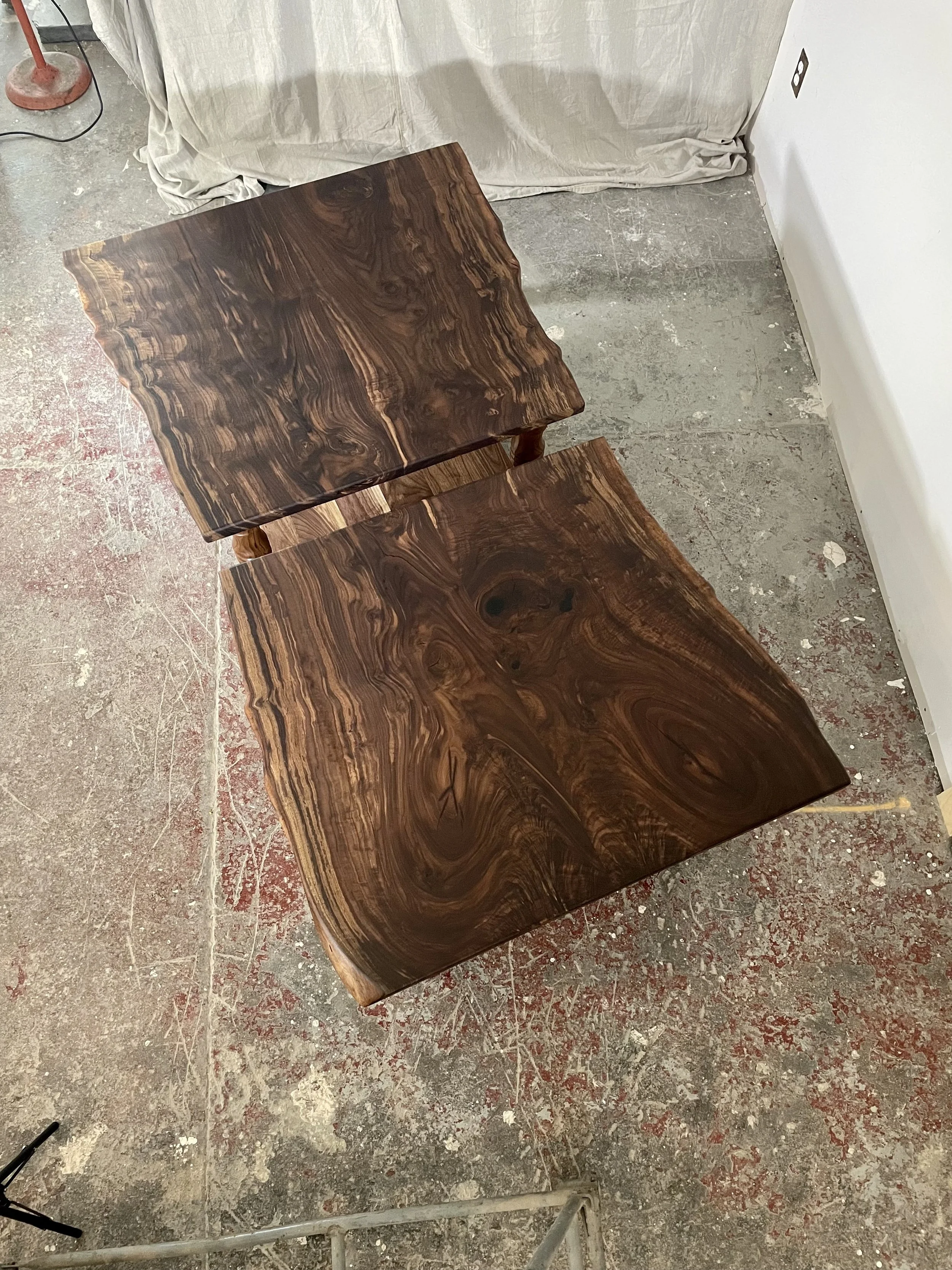 Two wooden tables with dark, swirling grain patterns placed on a concrete floor in a room under renovation.