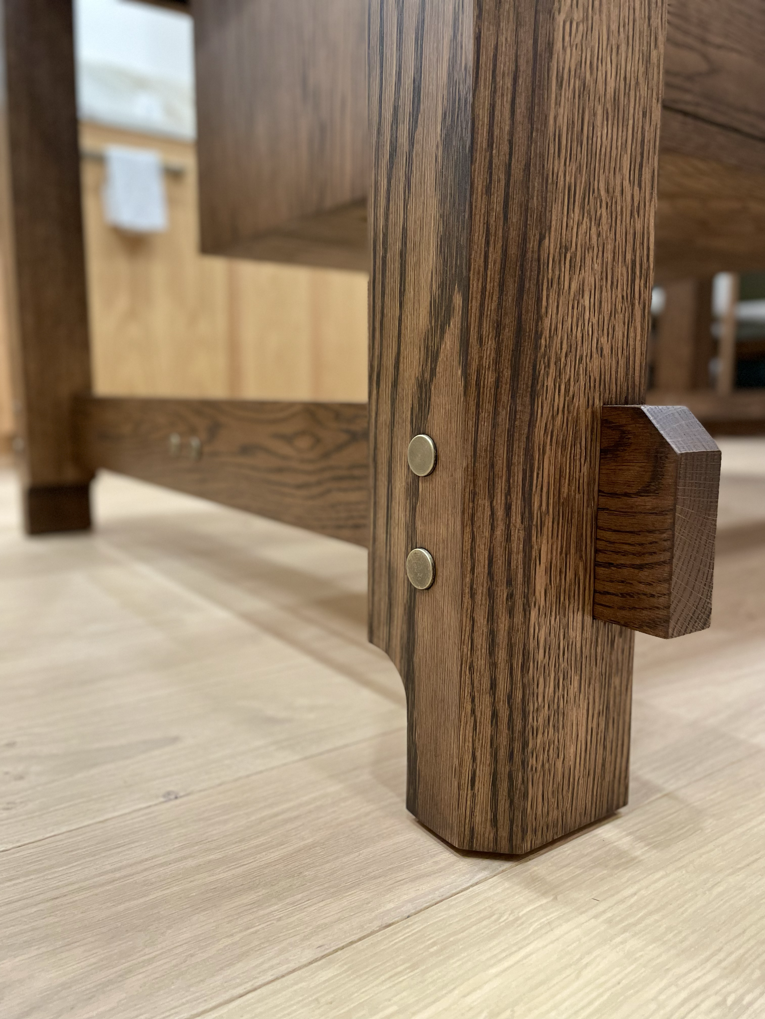 Close-up of a wooden furniture leg with metal bolts fitting into the frame, placed on a wooden floor.