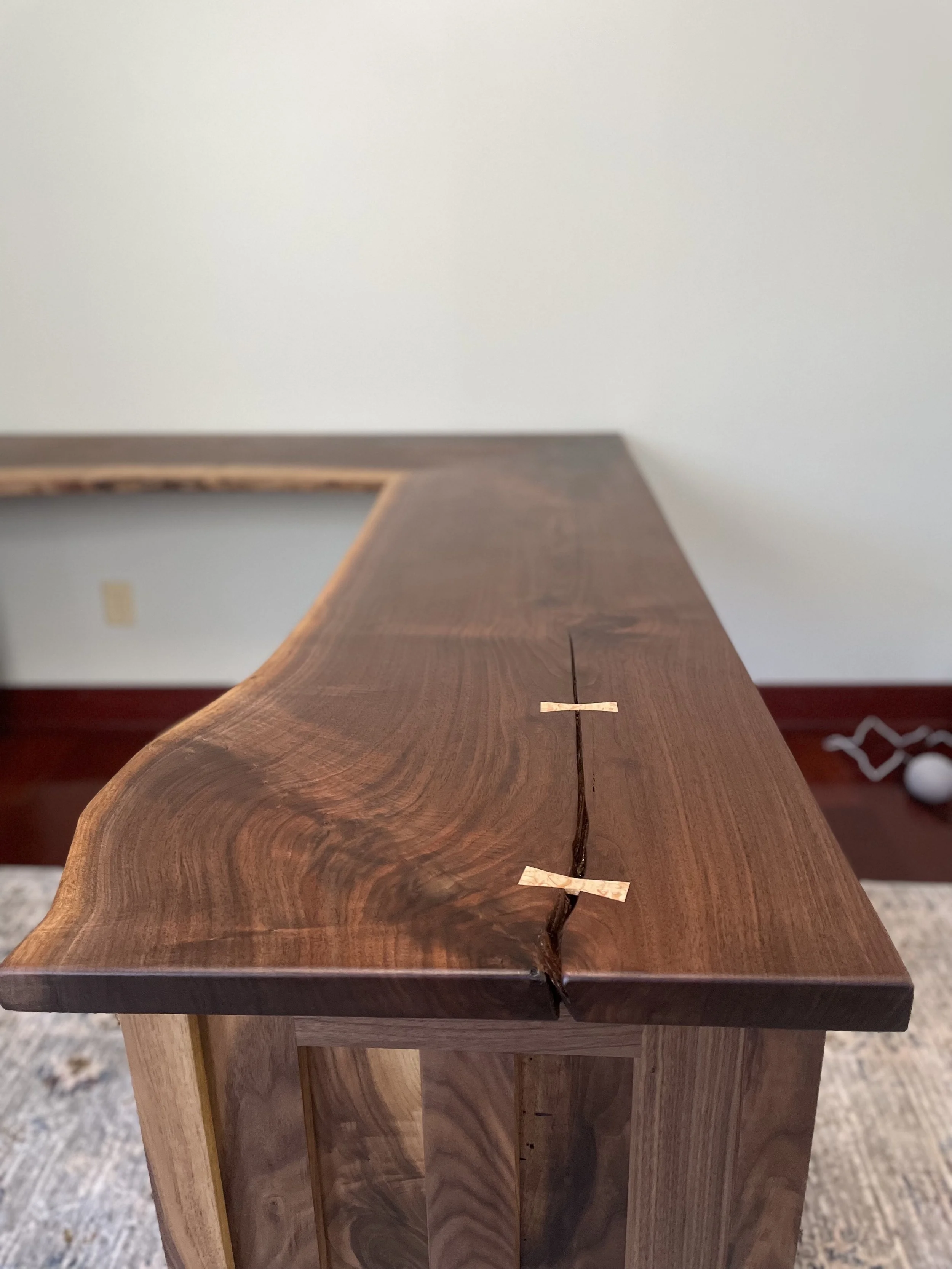 A wooden table with a natural edge and a large crack running through the center, held together with two small clamps.