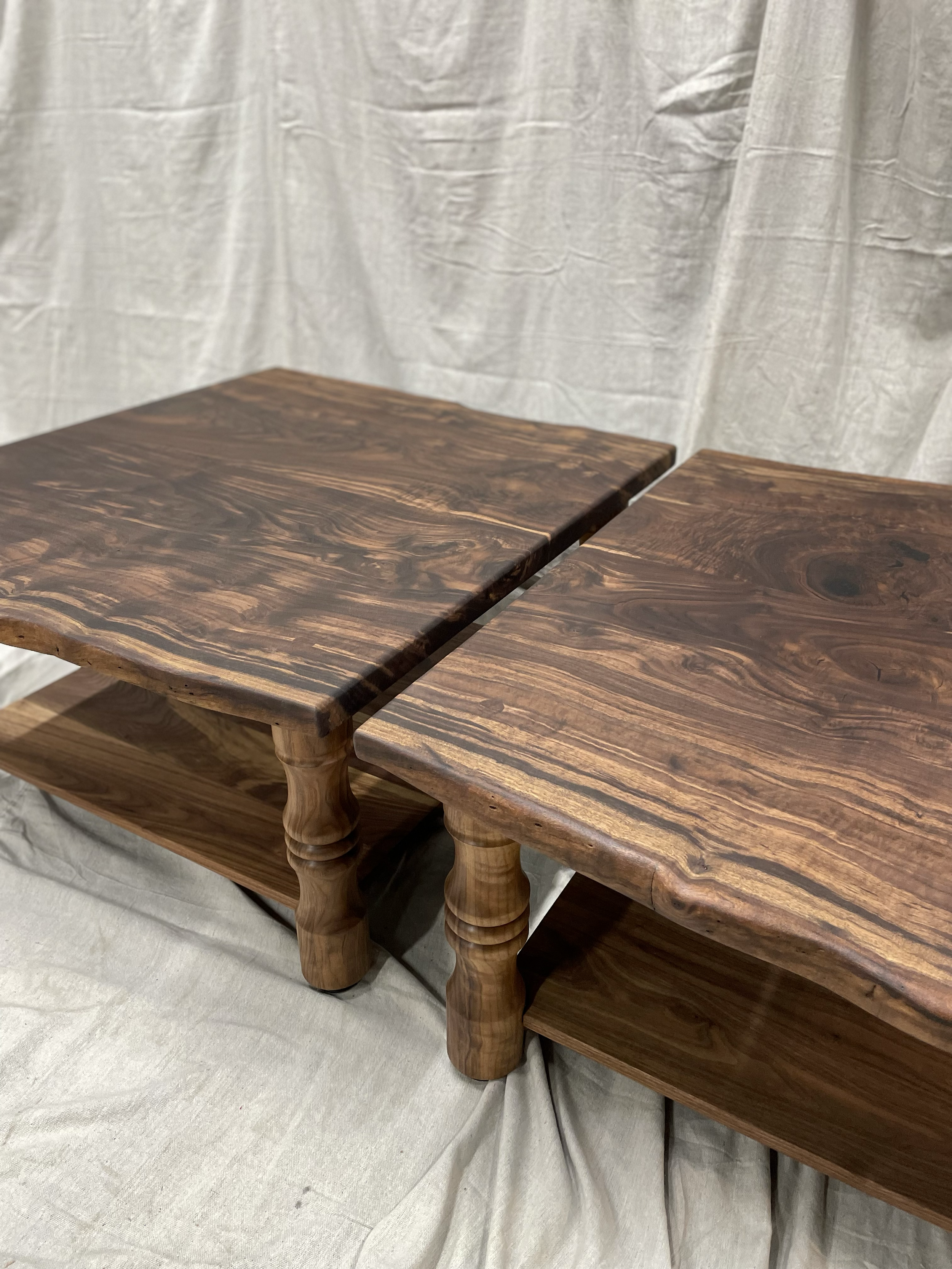 Two wooden coffee tables with turned legs and same grain pattern, placed side by side on a fabric surface.