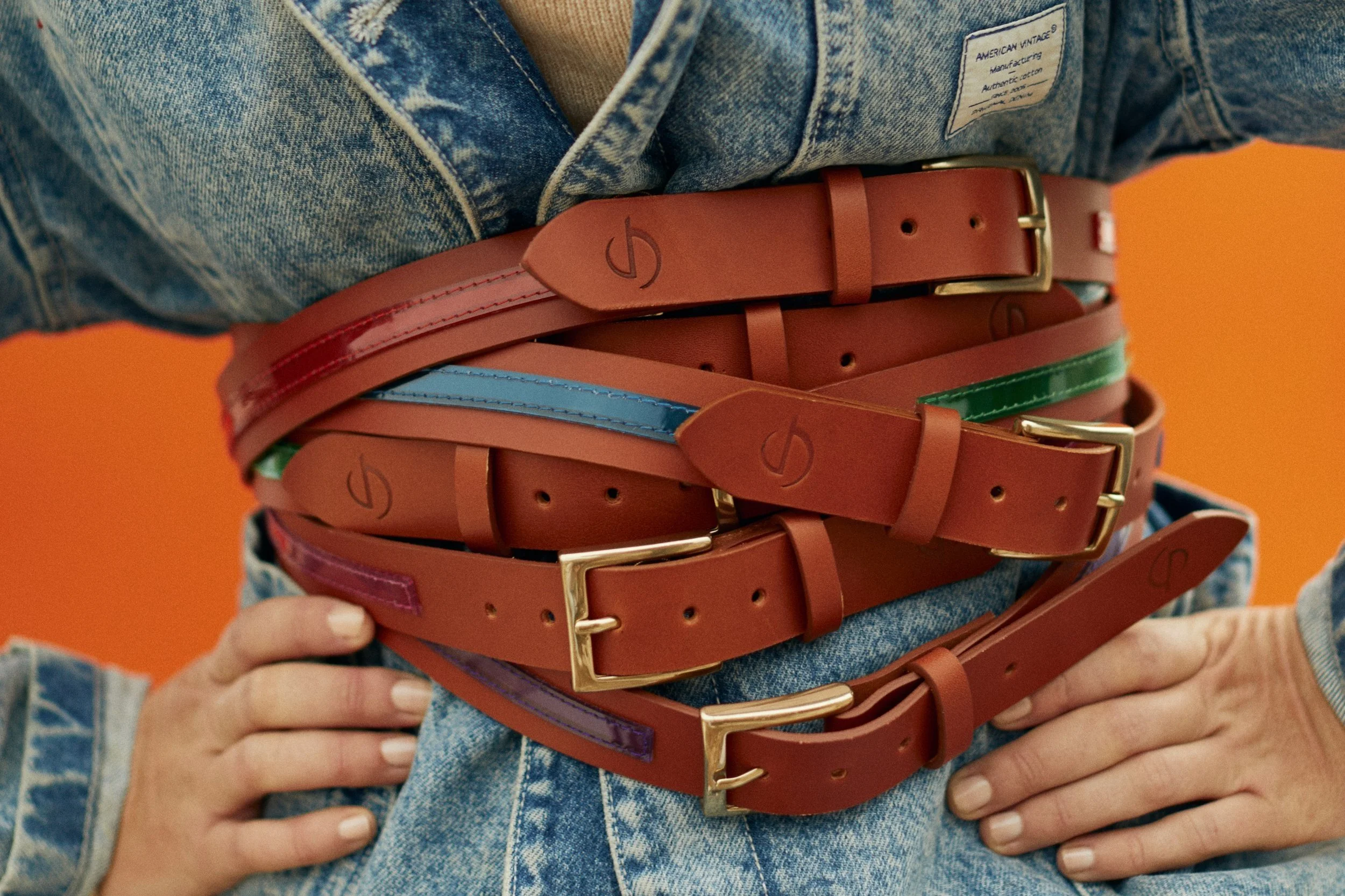 Une personne porte plusieurs ceintures en cuir de couleur marron autour de la taille, avec une veste en jean en arrière-plan.