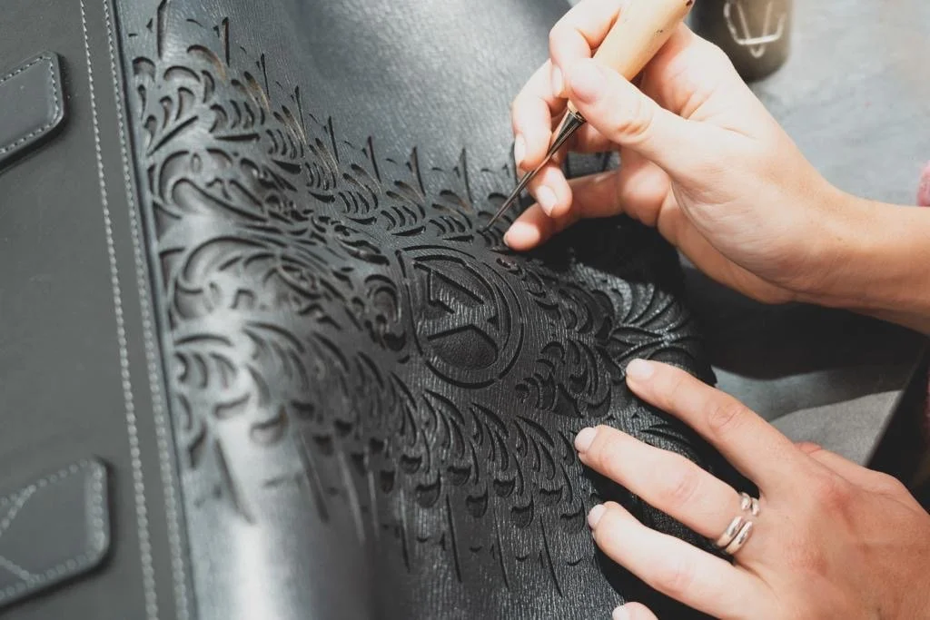 Une personne utilise un outil de gravure pour orner une surface en cuir noir avec un motif complexe et un symbole en son centre.