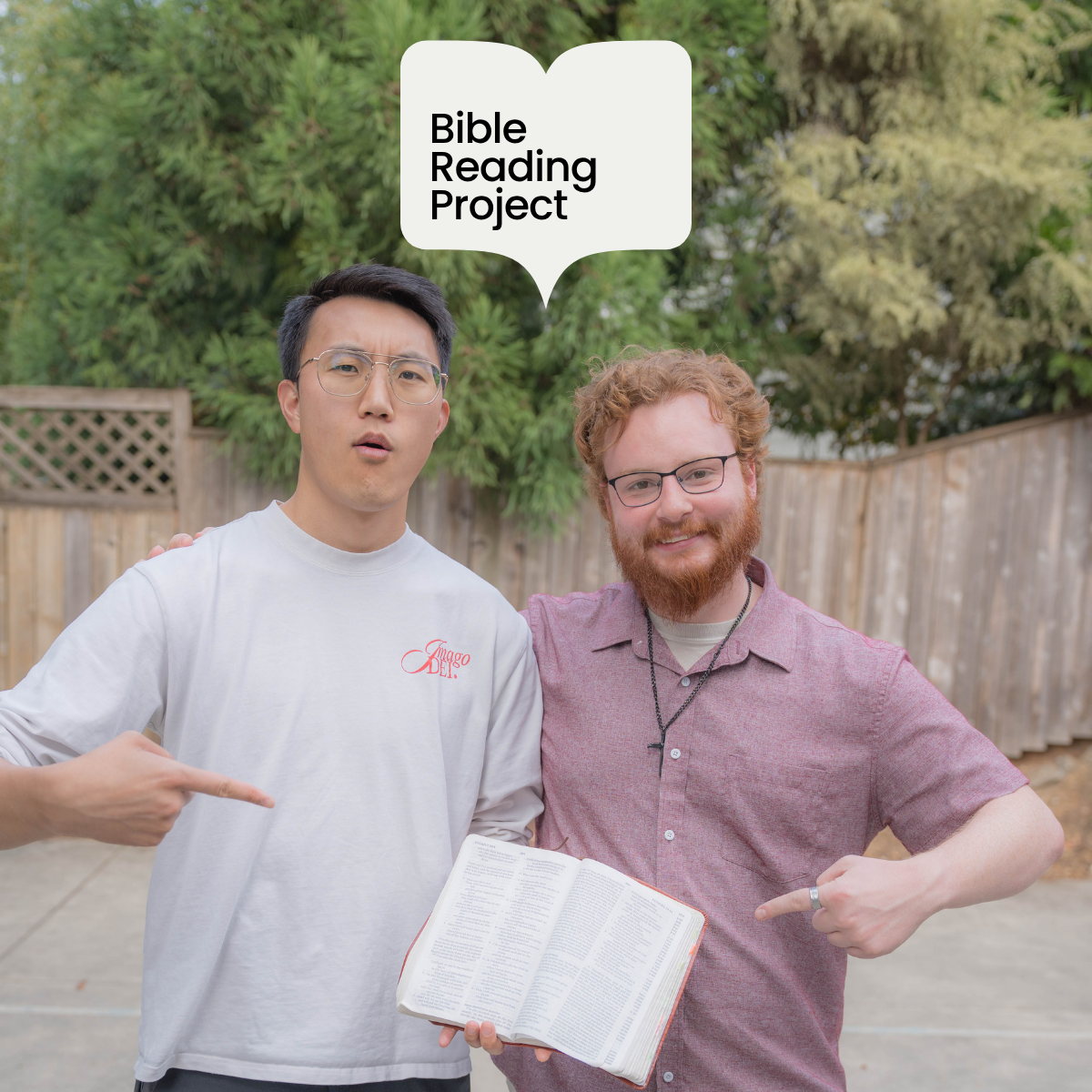 Two young men standing outdoors, one holding an open Bible and pointing at it, with a speech bubble above them that says 'Bible Reading Project.'