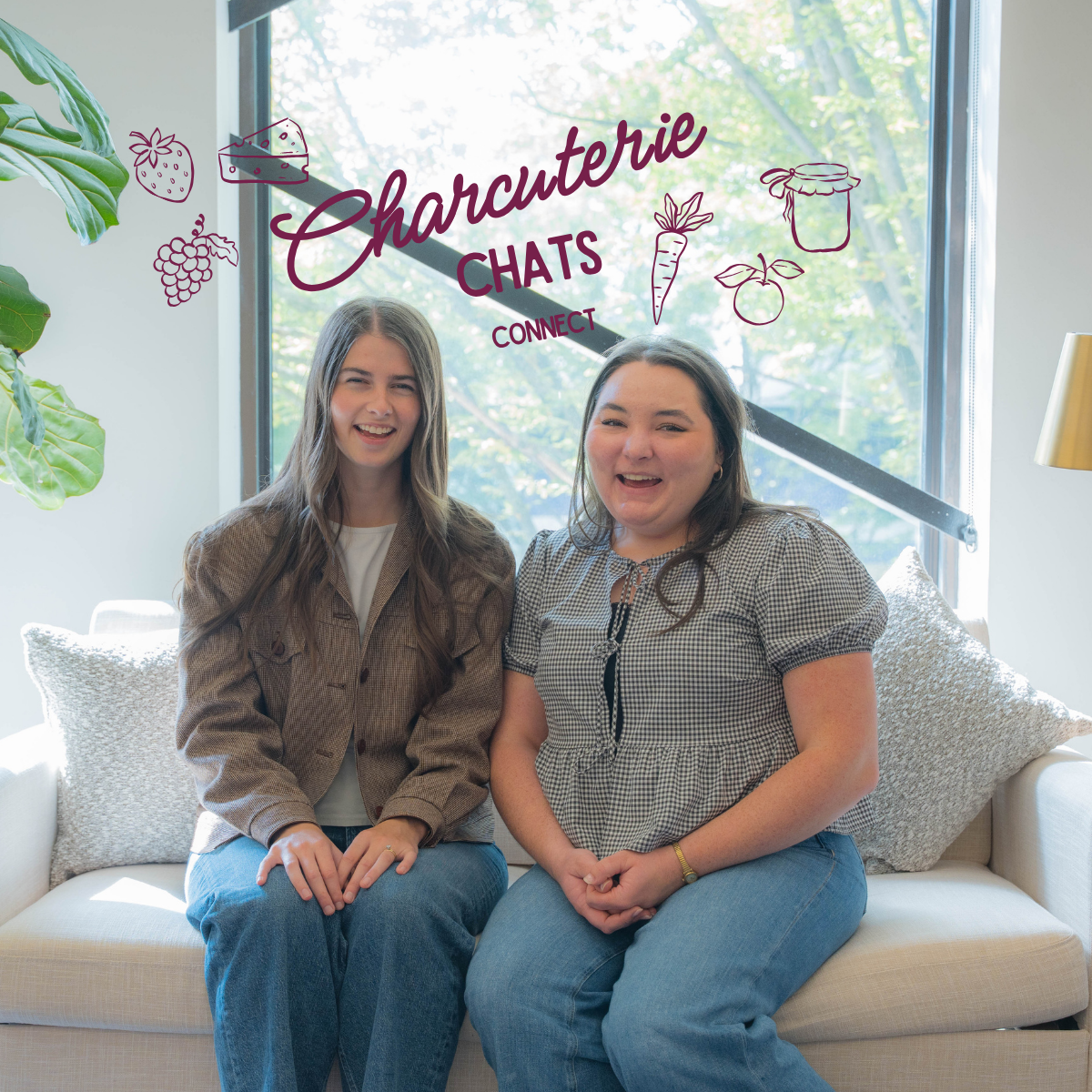 Two women sitting on a light-colored couch in a room with large windows and greenery outside, smiling at the camera. Overlaid text reads "Charcuterie Chats" with icons of strawberries, cheese, grapes, a carrot, a cherry, and a jar.