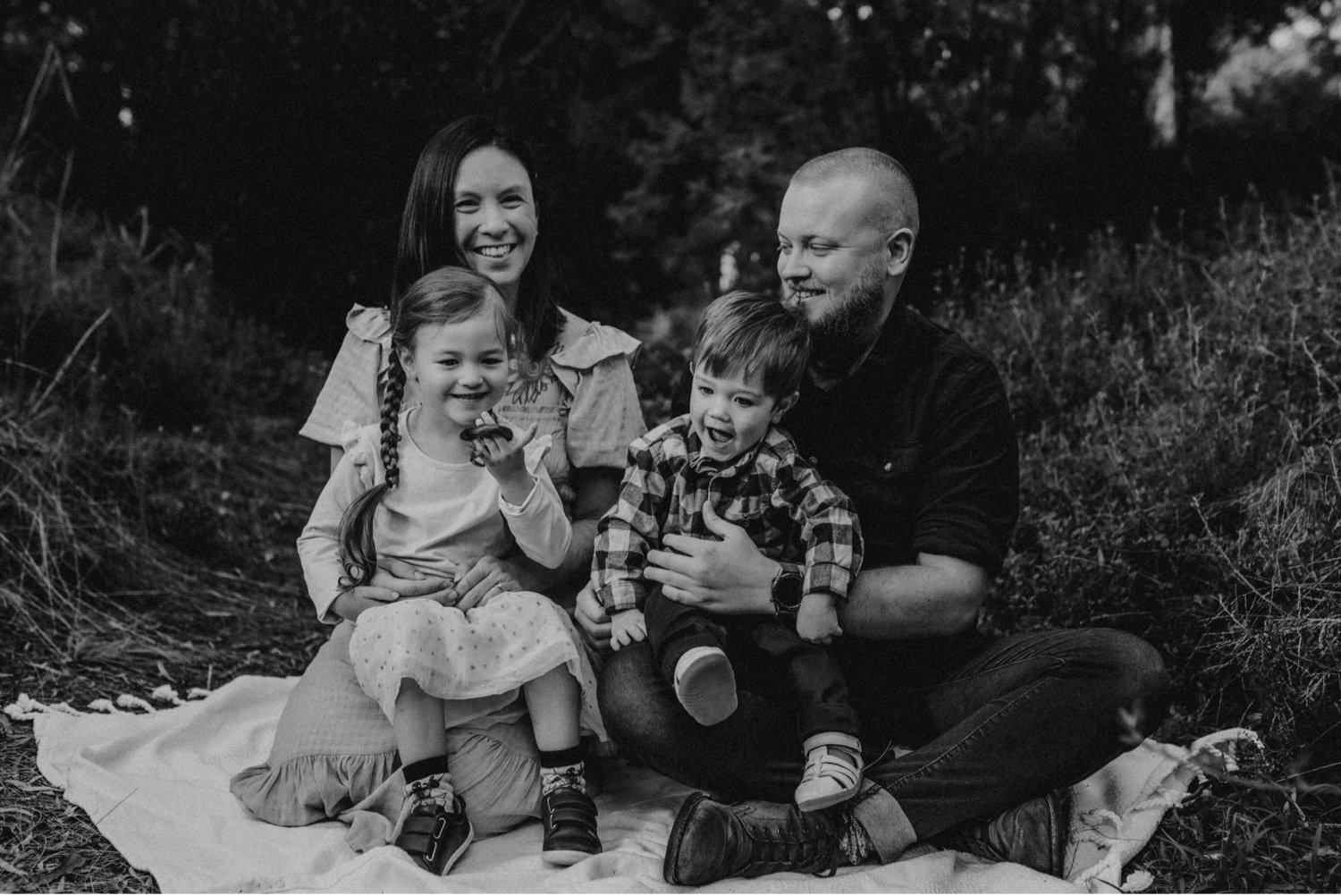 03_DTEV-9_Black and white family portrait of parents and two children. they are seating in a bush setting and laughing. .jpg