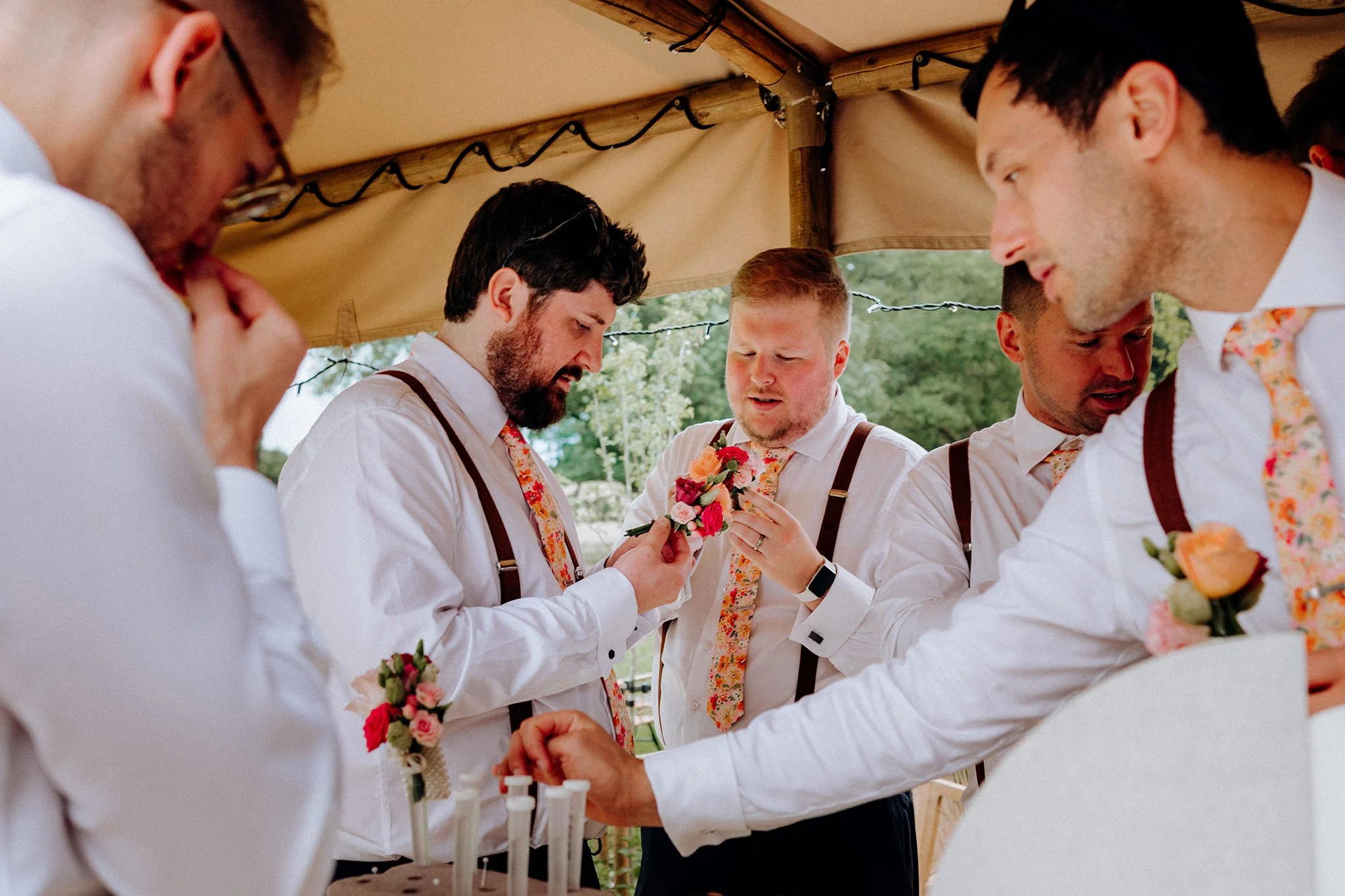 groomsmen putting buttonholes on at tipis at riley green