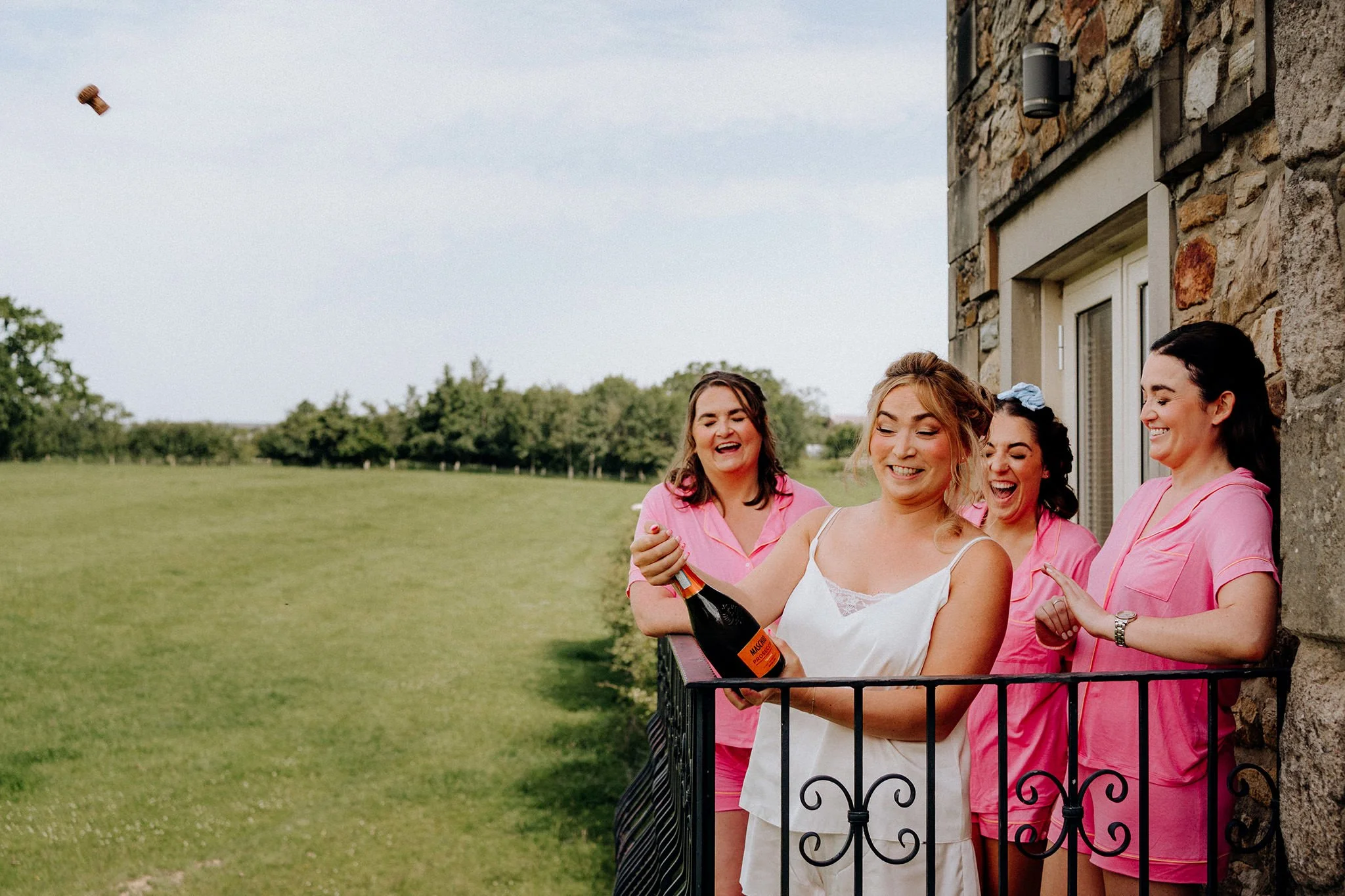 bride pops the cork off the champagne on the morning of her wedding