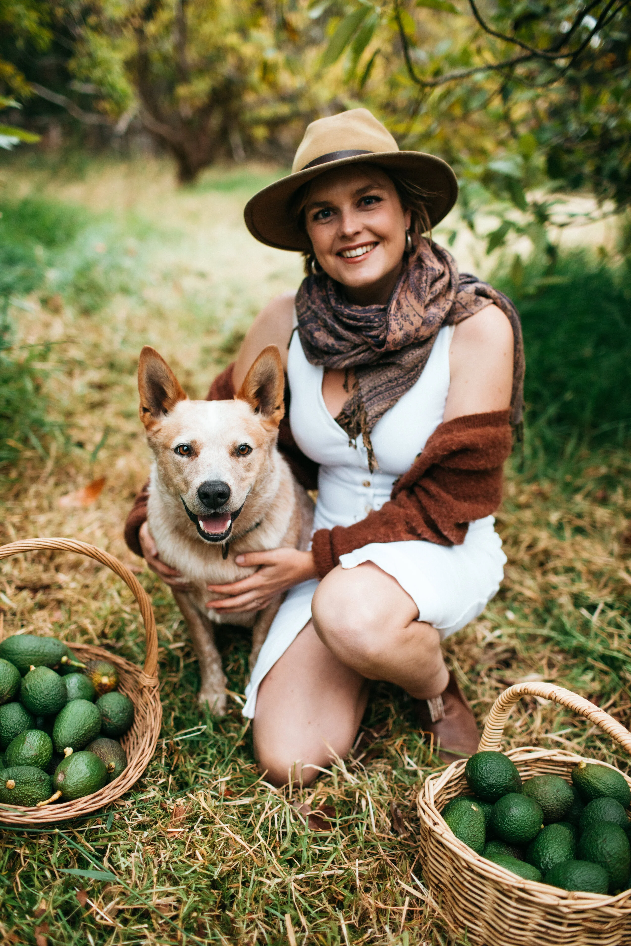 Vegan lady in orange jumper and hat standing in front of sustainable vegan home grown vegetable garden with seasonal produce. Olive Wood Vegan