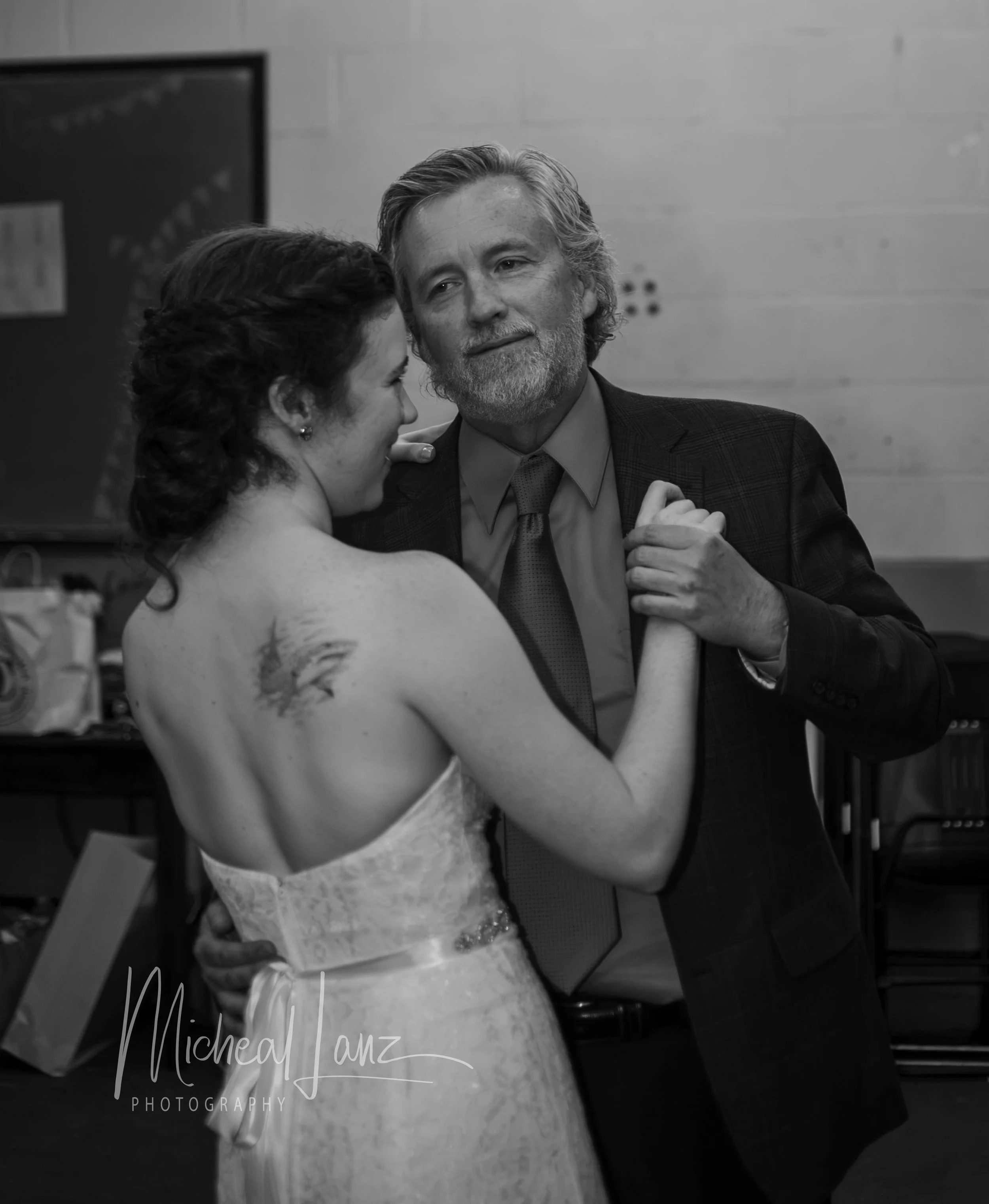 A fahter in a suit dancing with his daughter in a sleeveless dress at a wedding reception.