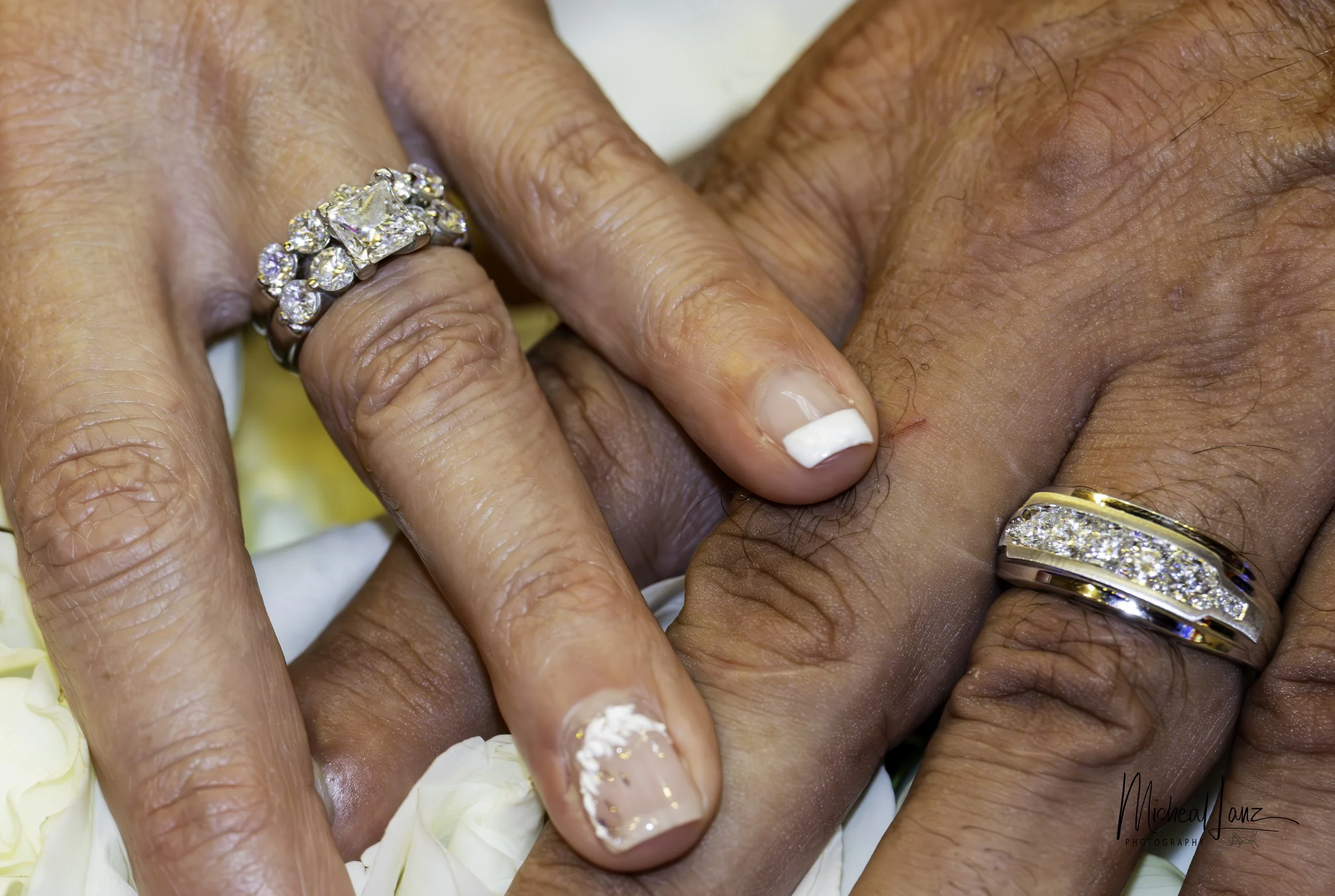 Close-up of multiple hands with wedding rings and nail polish, holding flower petals.