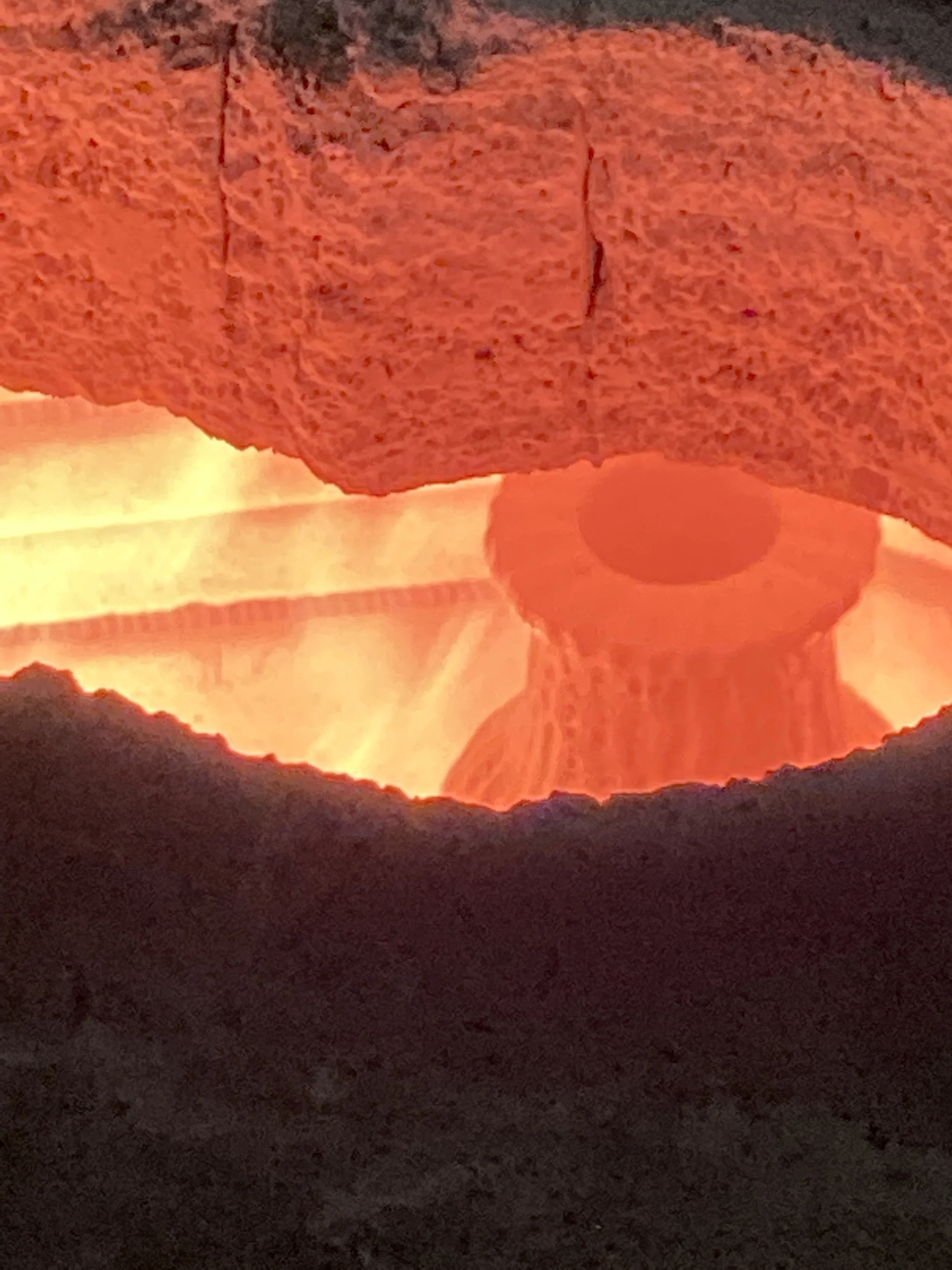A close-up of a glowing red hot kiln with a bright orange-red interior and a partially visible ceramic object inside.