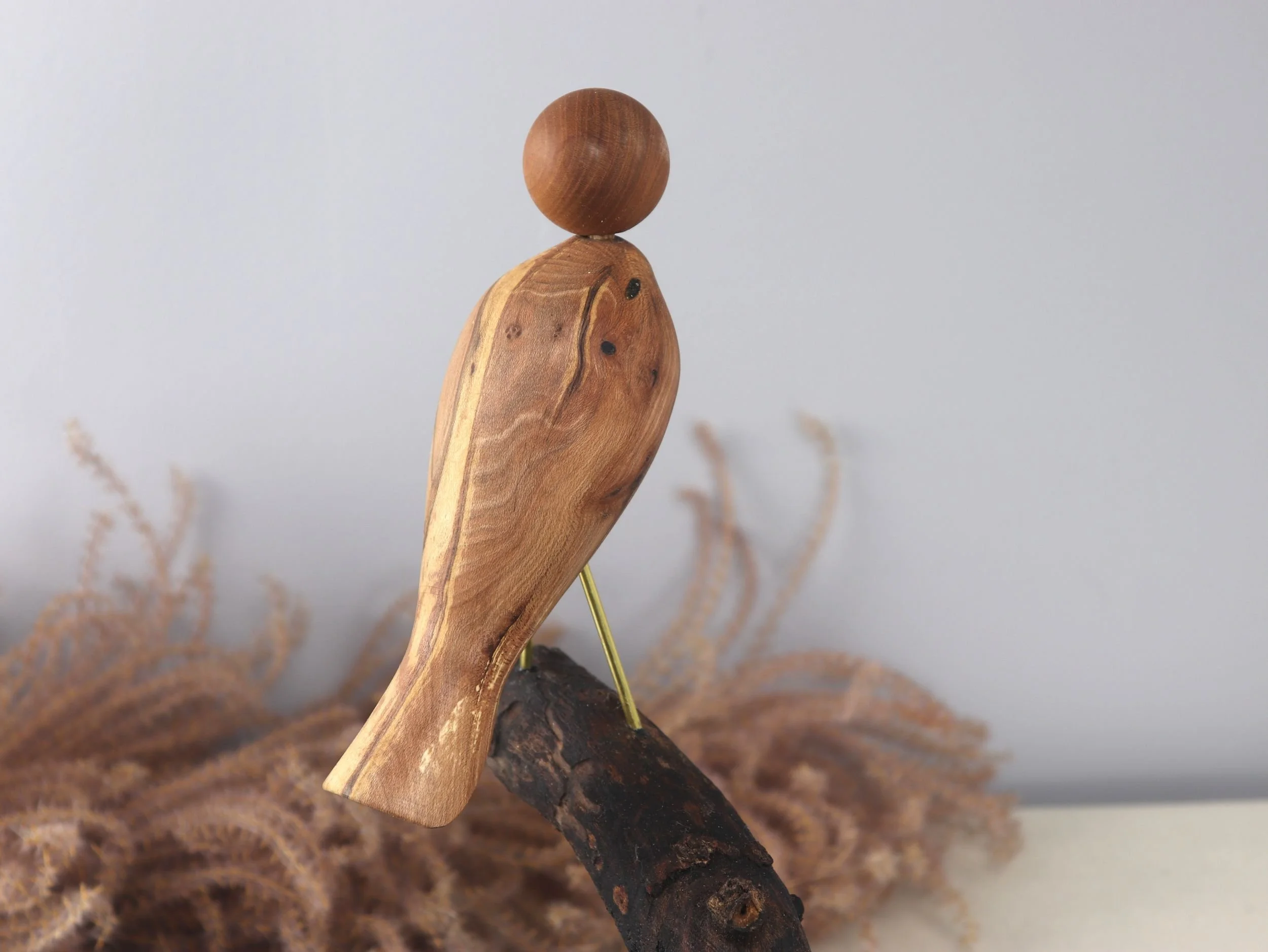 Final detail shot of handcrafted bird showing thoughtful forward gaze and natural wood craftsmanship