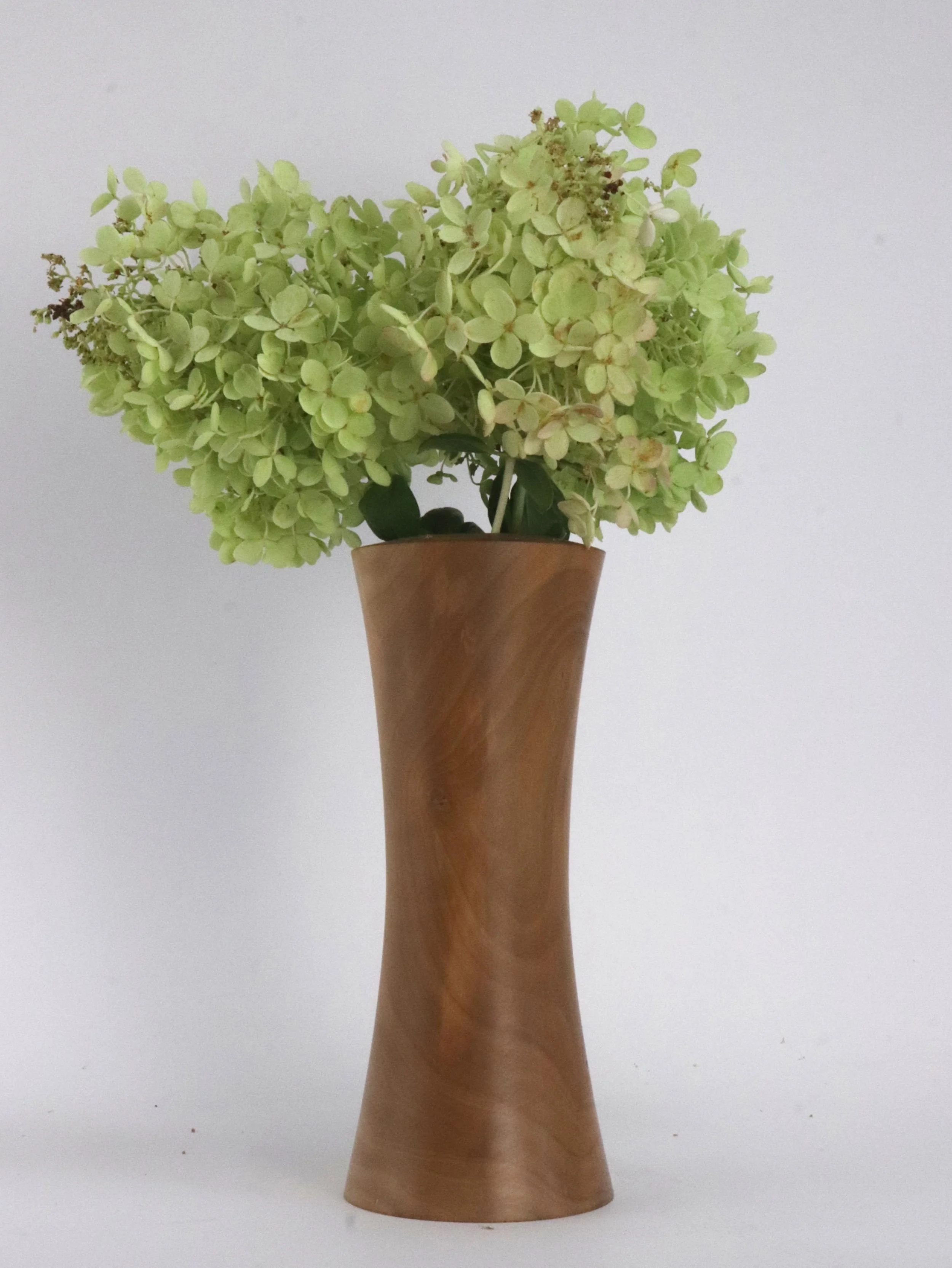 Unique pear wood hourglass vase with flowers displayed in elegant home interior decor setting