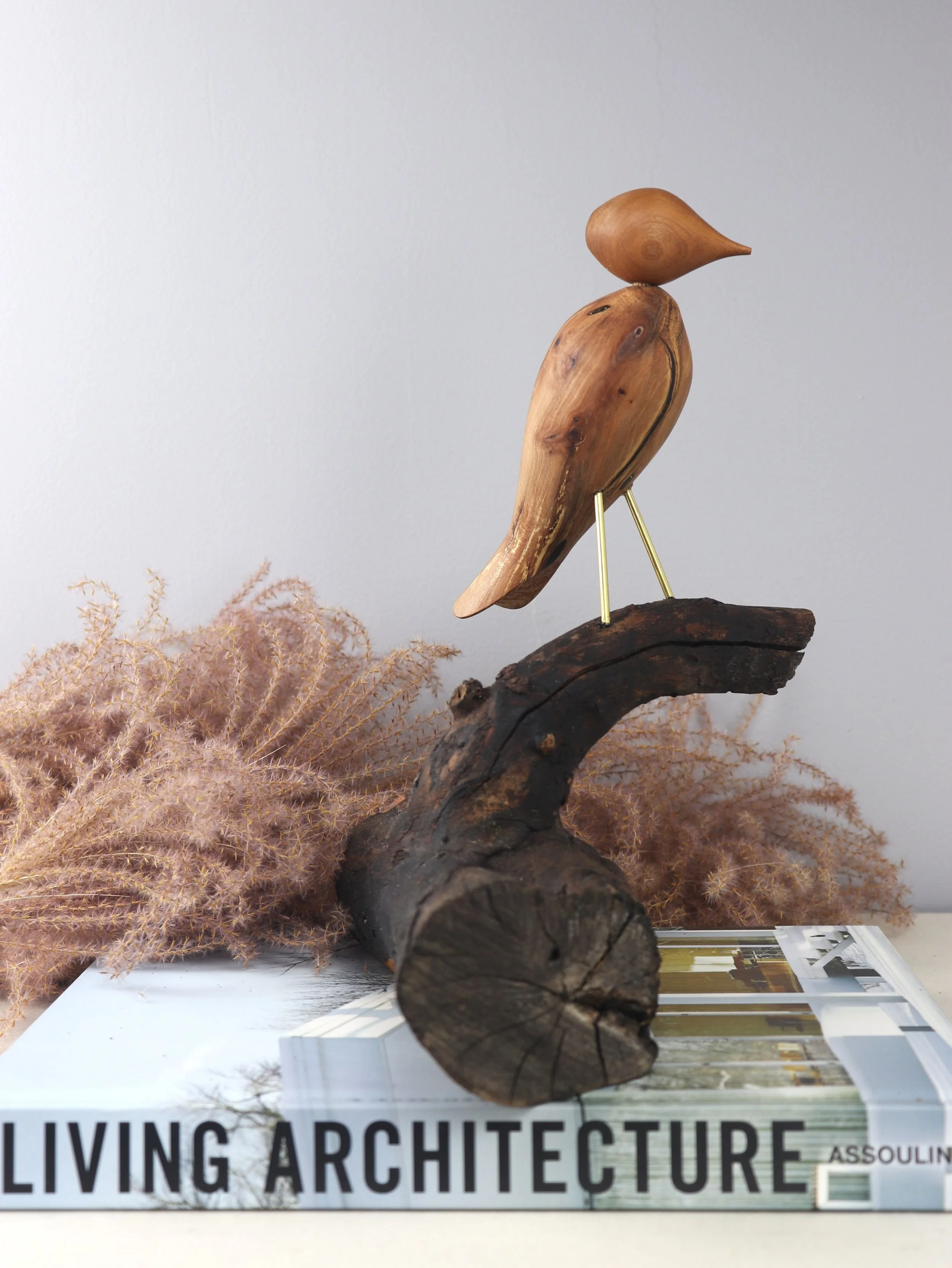 Detail shot of carved wooden bird perched on small dogwood branch extending from horizontal log base