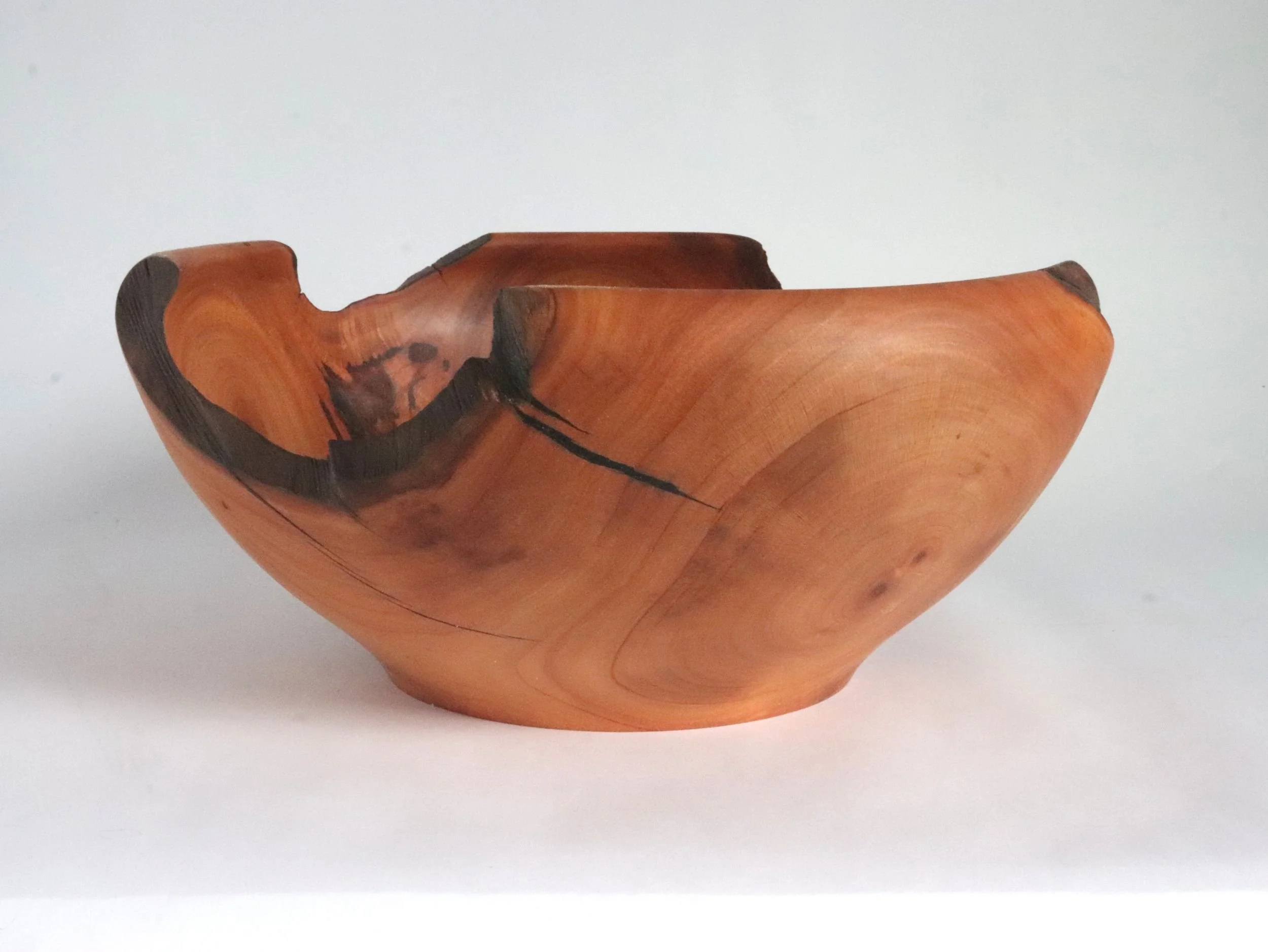 Handcrafted oval cherry bowl displaying natural wood grain convergence and irregular live edge rim following original tree branch lines