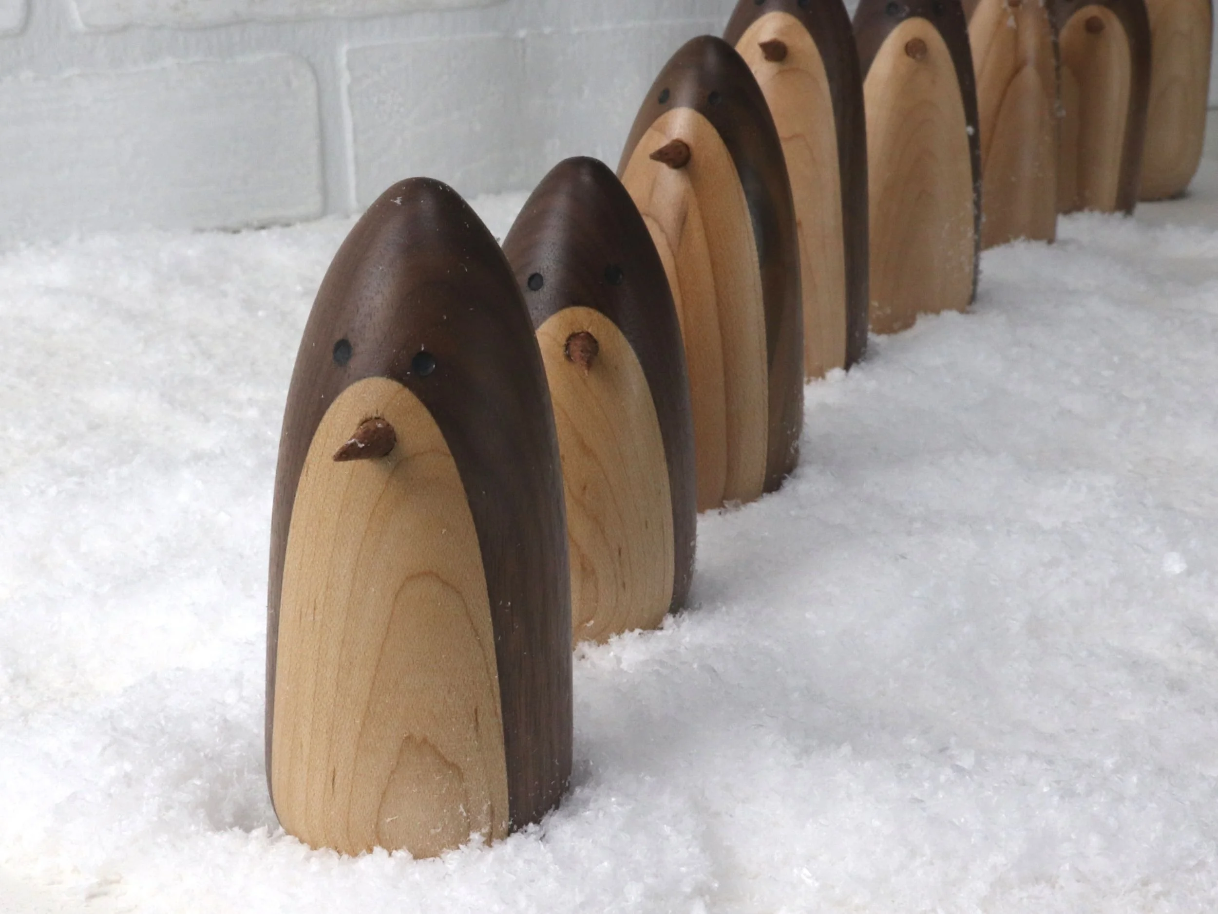 Whimsical handcrafted wooden penguins lined up in row like marching in snow display