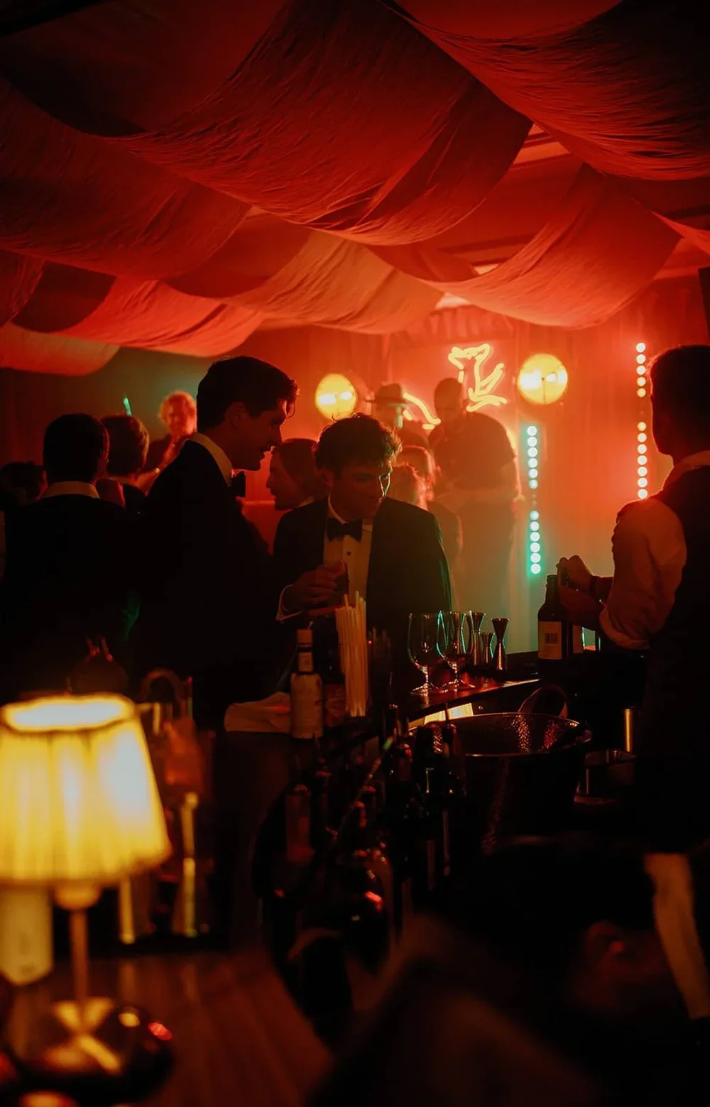 Luxury private party with guests enjoying cocktails at an evening reception beneath dramatic orange draping and atmospheric lighting.