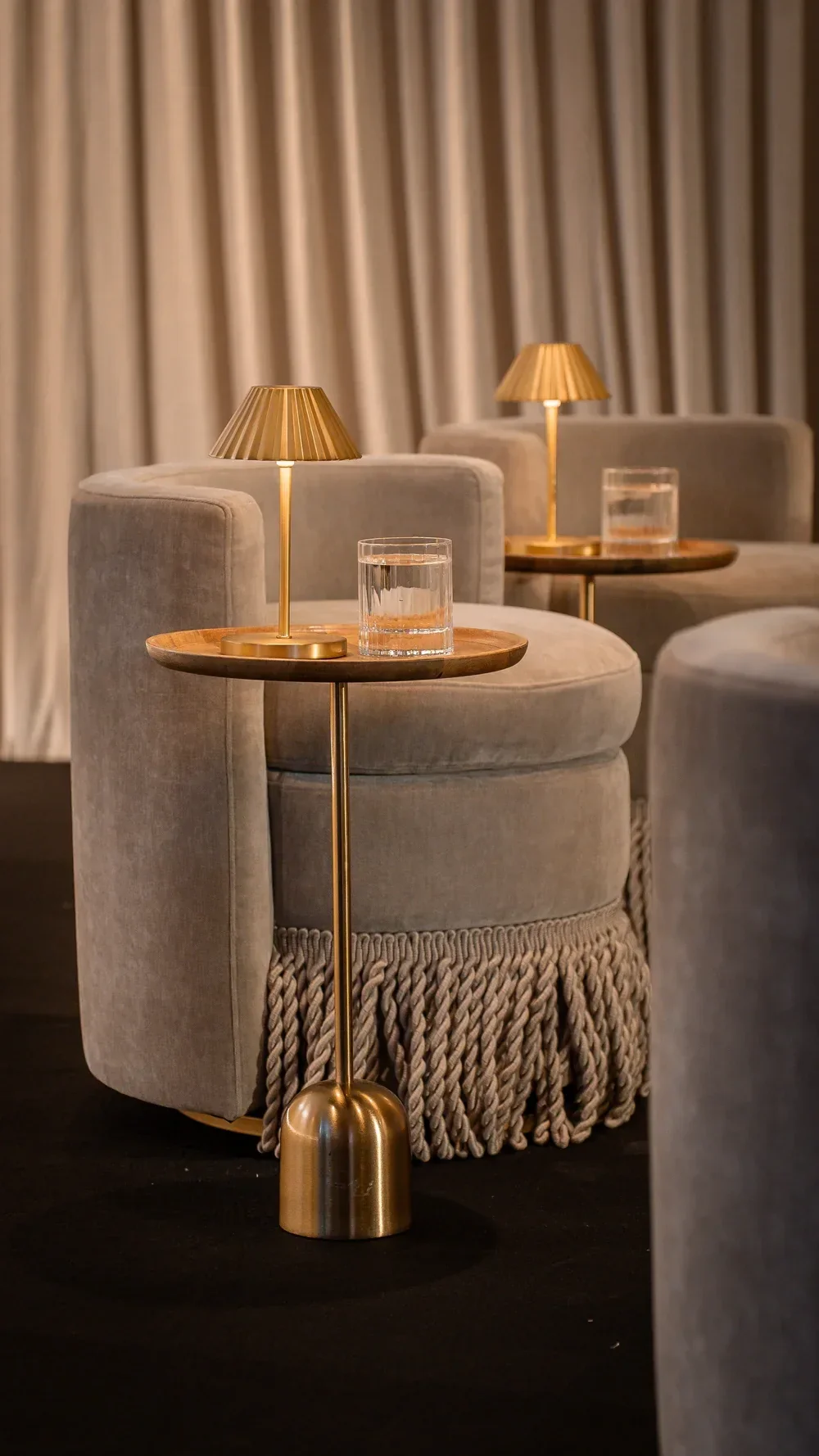 Conference lounge furniture hire featuring curved upholstered swivel armchairs with tasseles, brass side tables and decorative table lamps.