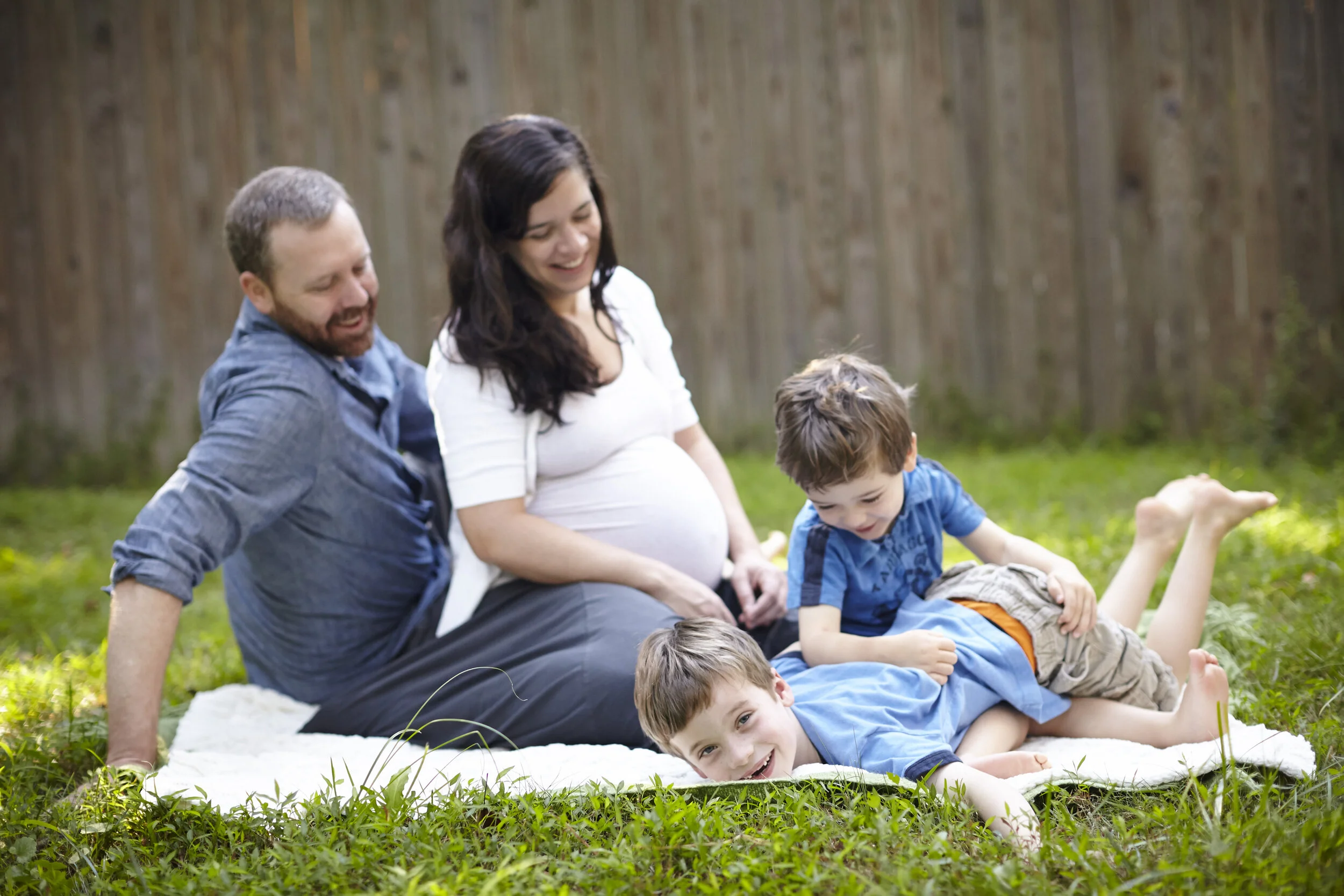 kids playing in grass next to pregnant mom