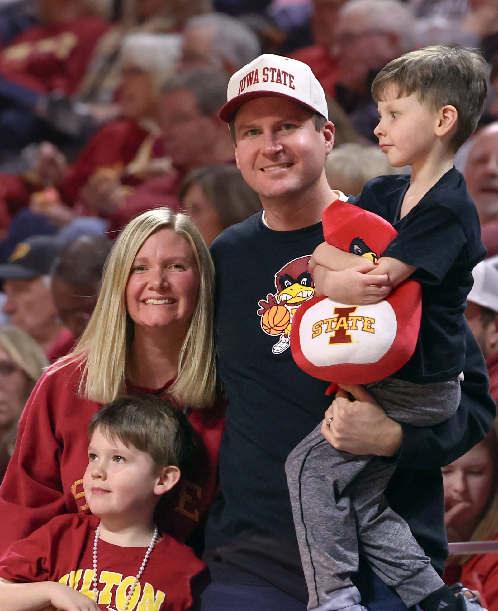 A family of four at a sports event, wearing Iowa State University apparel, with a crowd in the background.