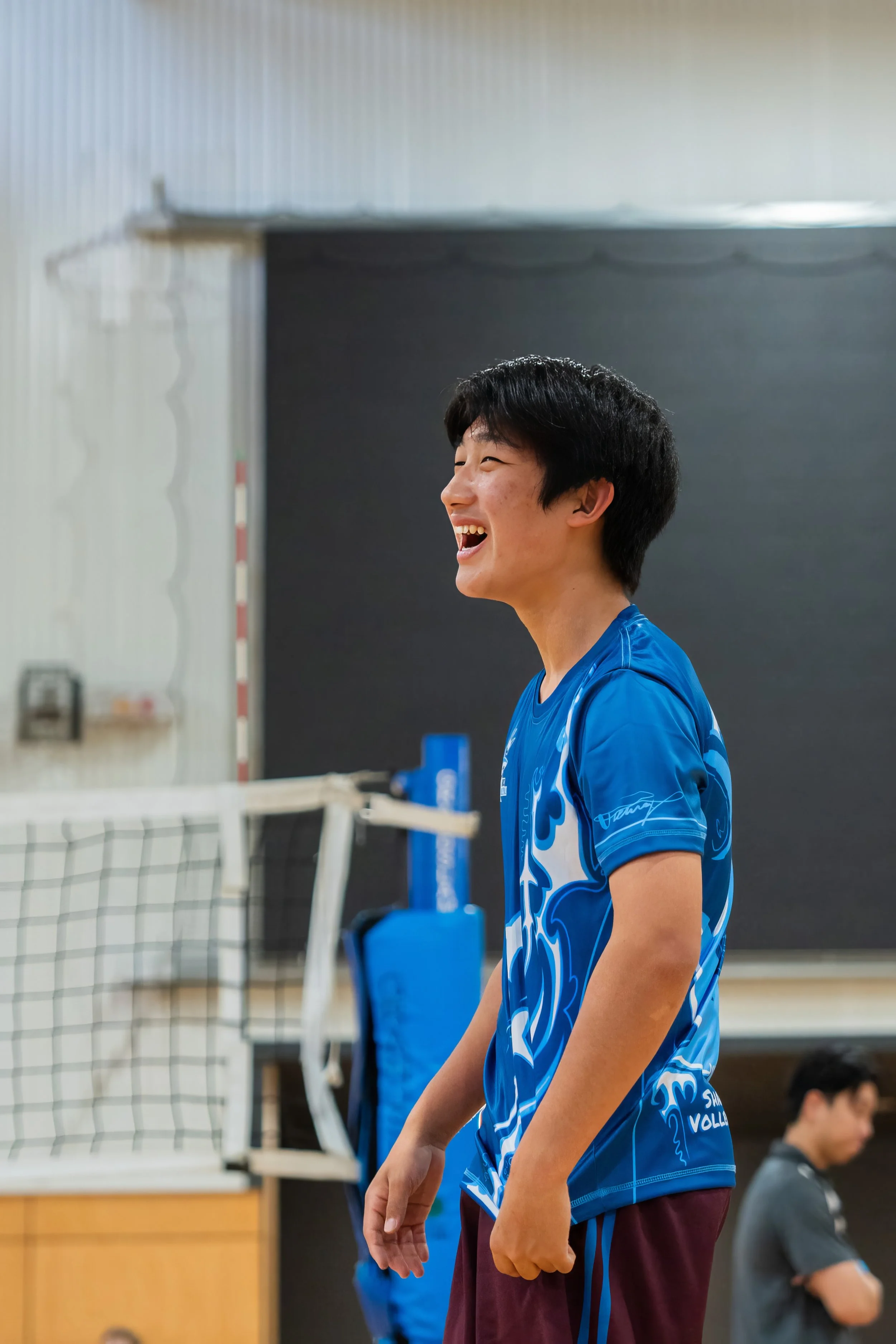 Young man in a blue sports jersey laughing on an indoor volleyball court