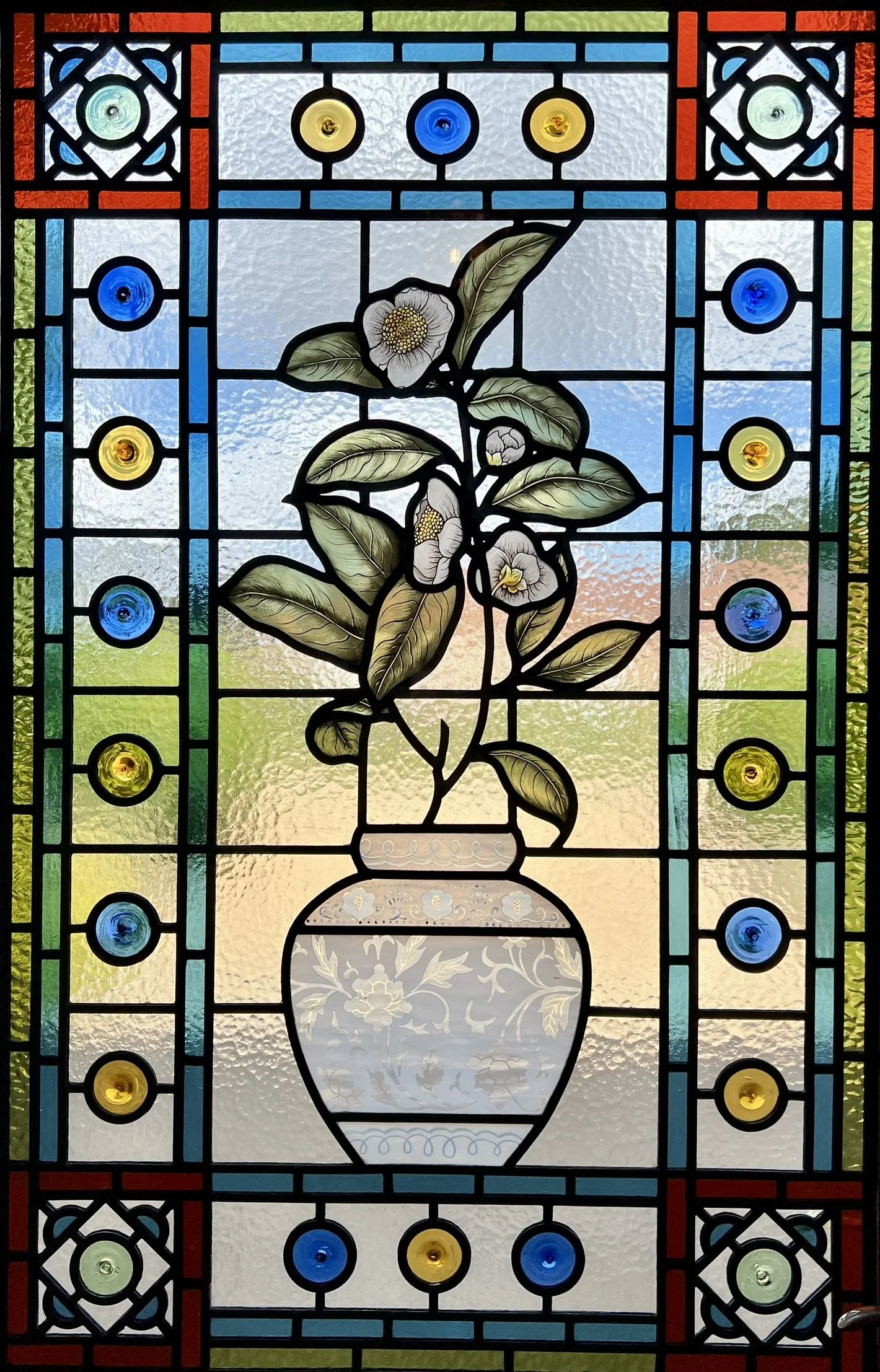 stained glass window in Victorian style, featuring an intricate vase design with flowers, leaves and mouth-blown roundels
