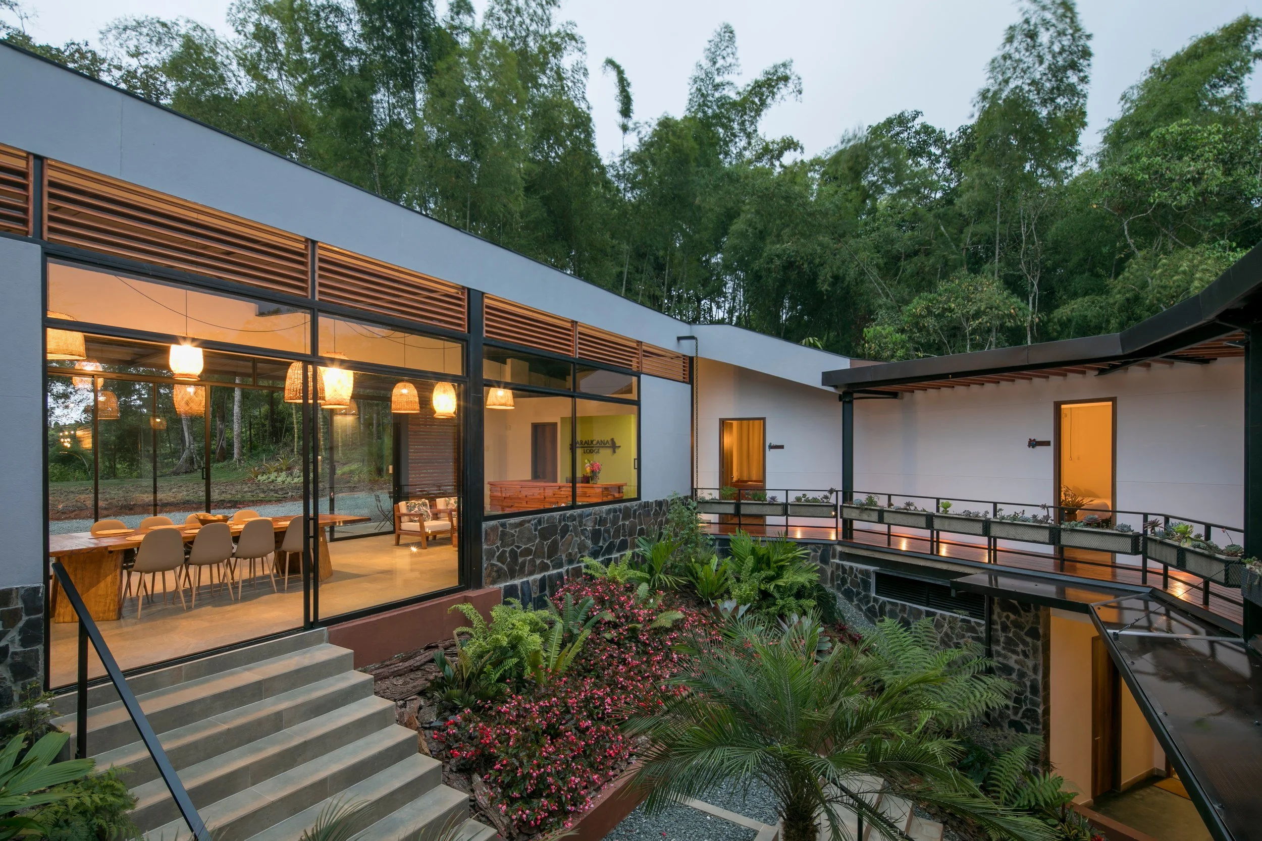 Araucana Lodge’s planted courtyard at dusk, with palms, ferns, and flowering shrubs beside the warmly lit dining room.