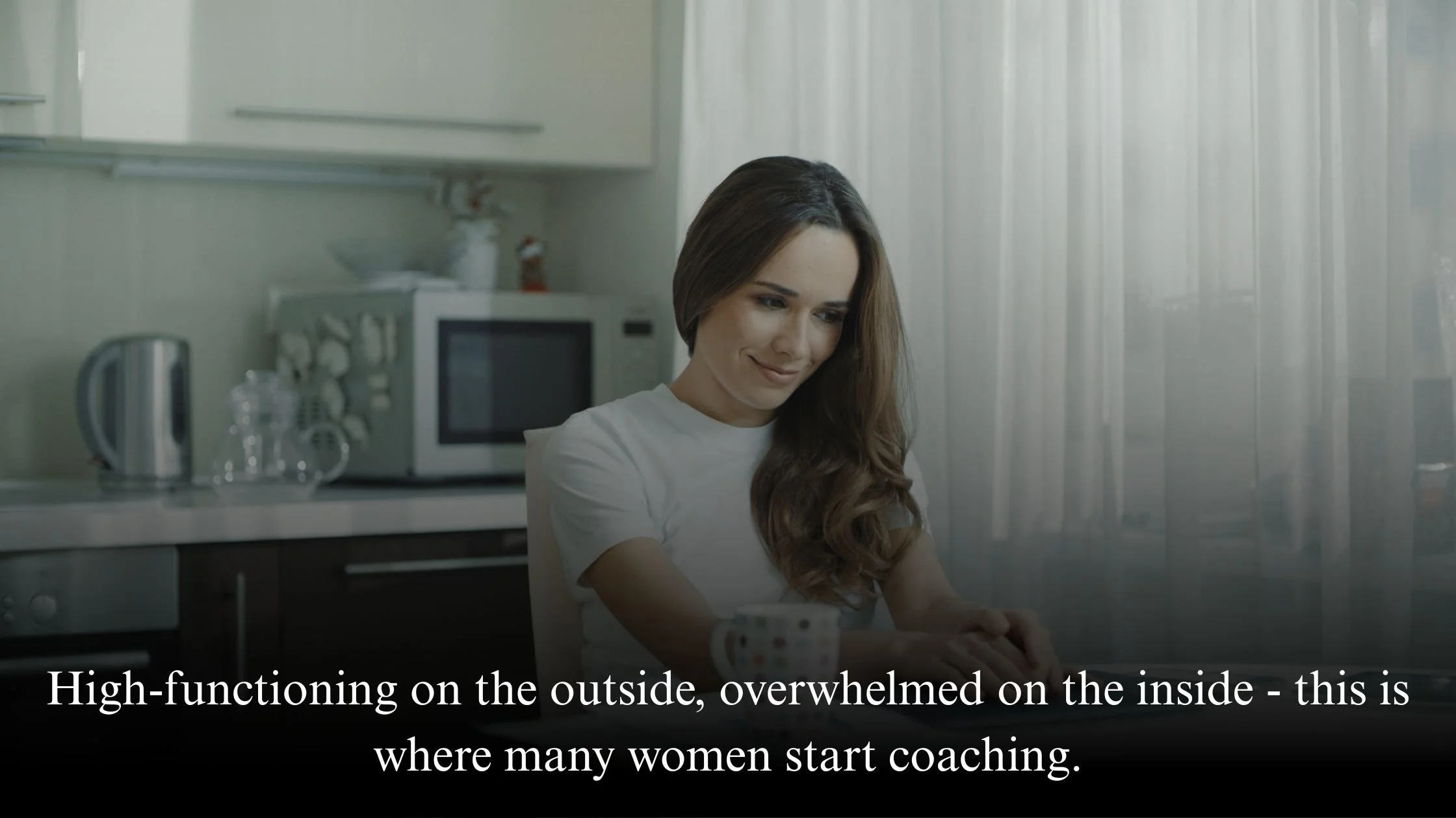 Thoughtful woman sitting at a kitchen table in soft natural light, representing a high-functioning woman feeling overwhelmed internally.