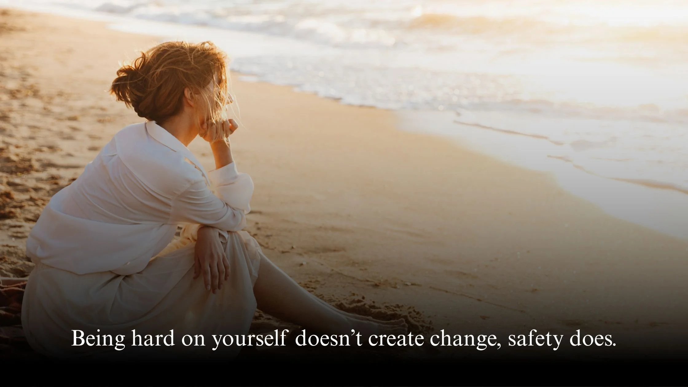 Midlife woman sitting quietly by the sea, reflecting calmly instead of judging herself