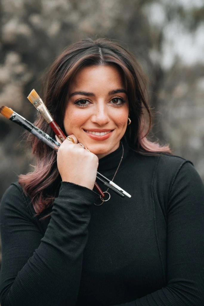ileyna Witenstein, art teacher, smiling and holding paintbrushes
