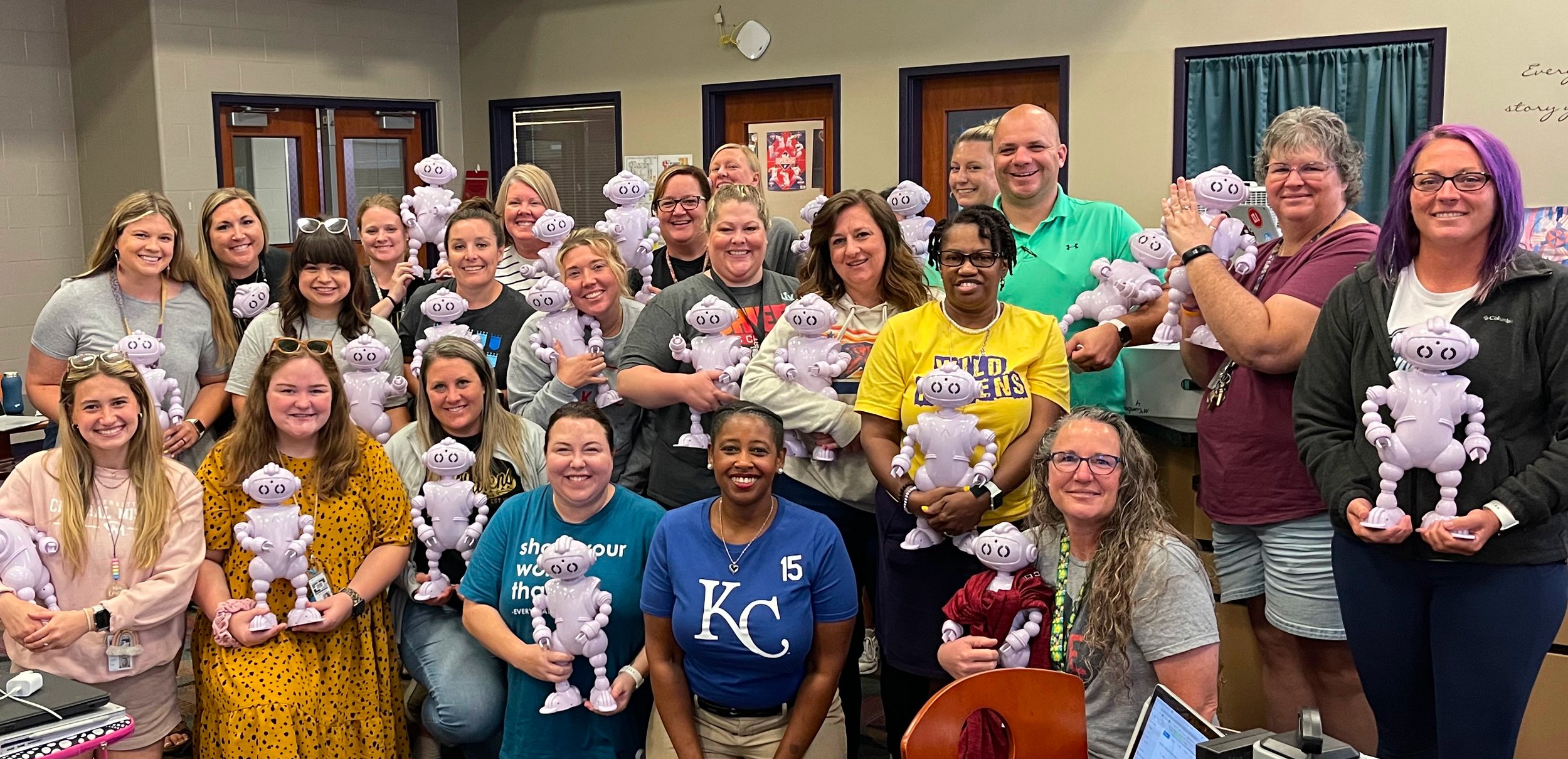 Group of people holding identical purple robot toys, smiling, in an indoor setting.