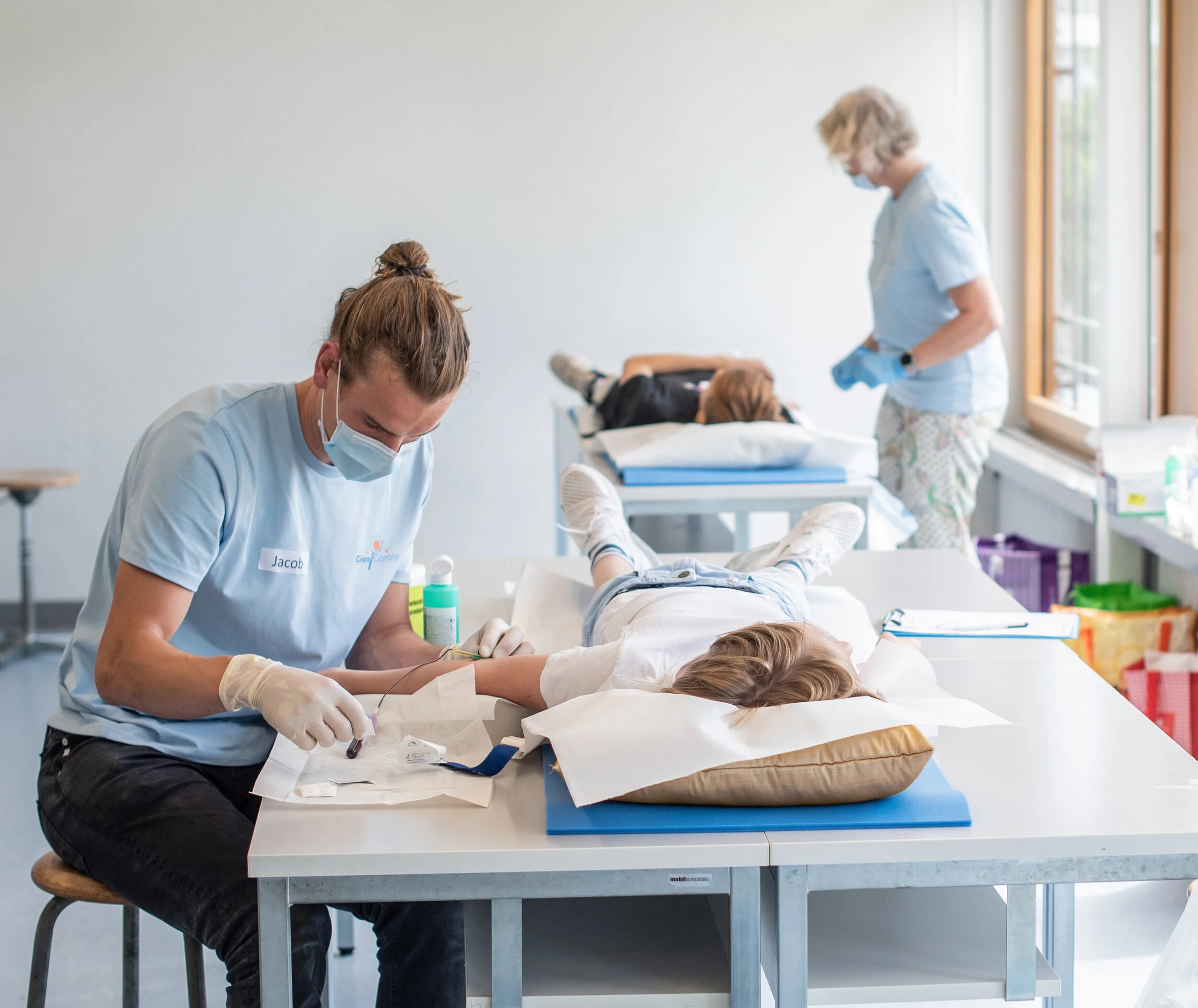Ciao-Corona team takes blood from the test persons. Several students can be supervised at the same time. The blood collection takes place in gymnasiums, singing halls or other suitable premises of the schools
