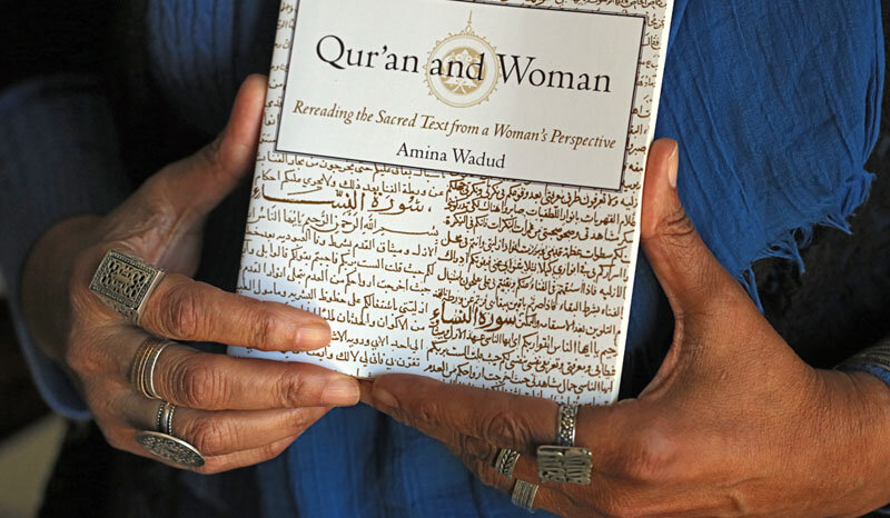  Wadud holds a copy of her book, “Qur’an and Woman.” The calligraphy on the cover was copied from Quaranic texts about women.   Photo Credit: Tom Levy. 