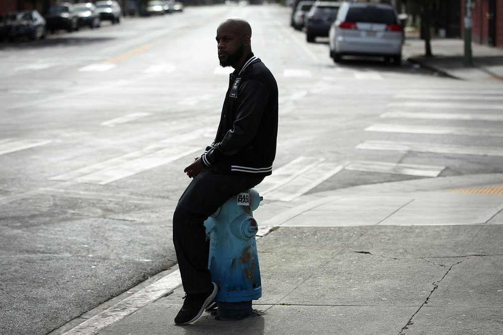 Tyson sits on a hydrant at the corner of 14th and Peralta streets where the mural is painted on the side of a corner grocery store.