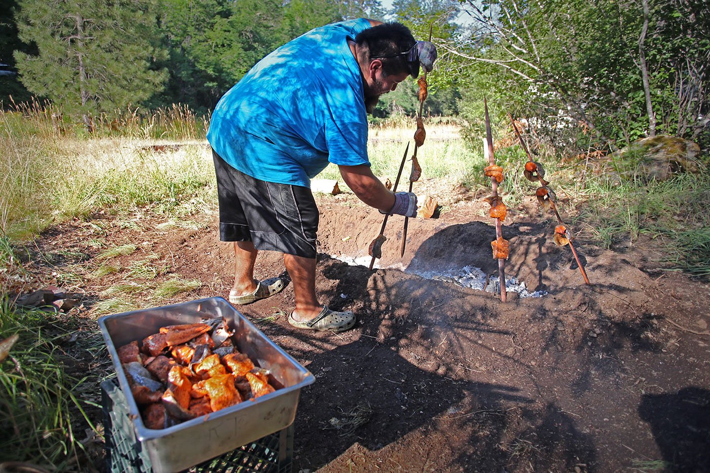  Shasta-Trinity National Forest — Kyle Brown (Hupa) prepares salmon brought from the Hoopa Valley Reservation over a fire. July 11, 2022. Tom Levy/The Spiritual Edge 