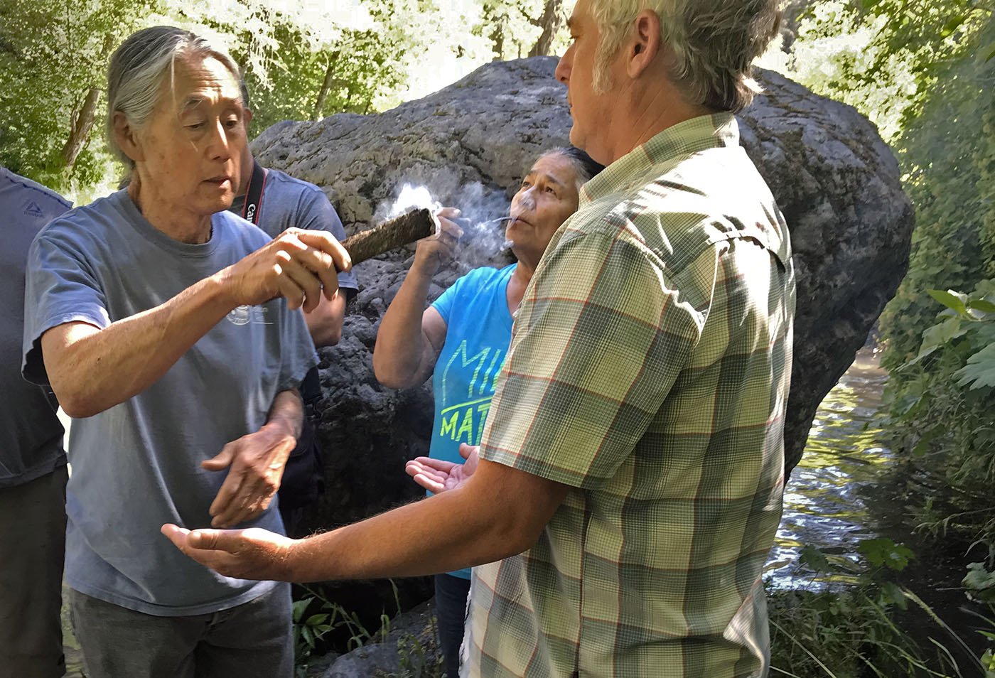  Shasta-Trinity National Forest, CA — Mark Miyoshi waves the smoke of a smudging root around Matt Johnson, an environmental scientist with the California Department of Fish and Wildlife. June 27, 2022. Judy Silber/The Spiritual Edge. 