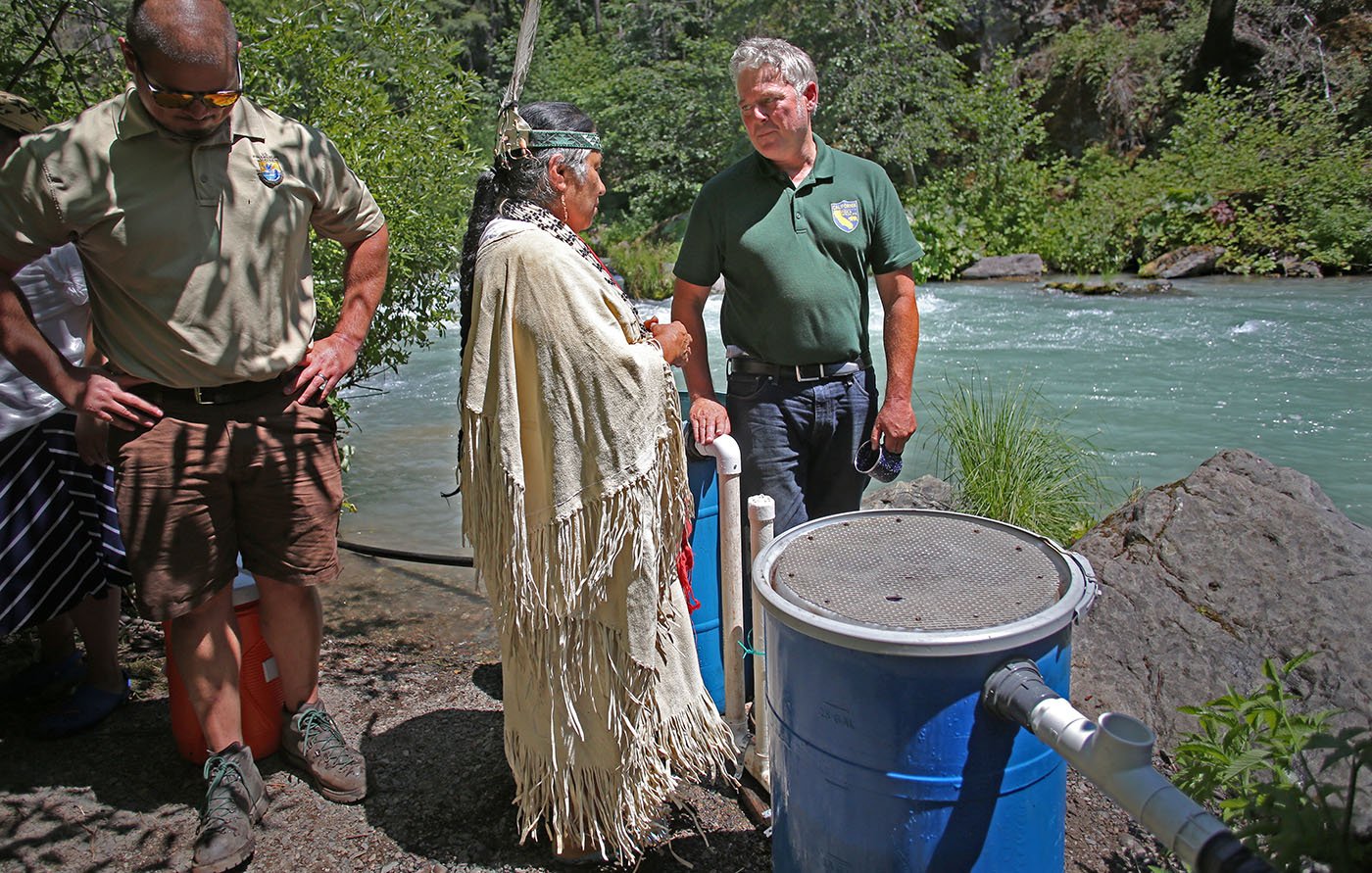  Shasta-Trinity National Forest — Chief Caleen Sisk speaks with CDFW environmental scientist Matt Johnson next to an incubation barrel that will protect the winter-run eggs until they hatch and the young salmon swim out into the river. July 11, 2022.
